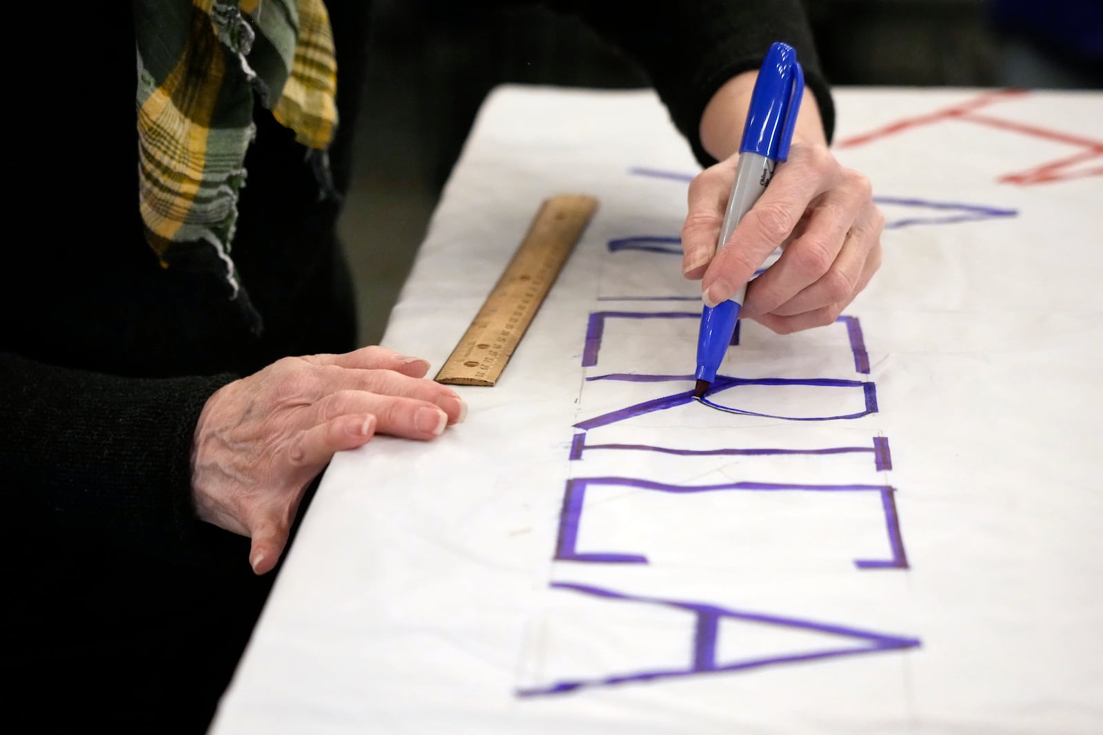 Ann Kourelis works on a protest sign during a meeting of NC Forward in High Point, N.C., Tuesday, Jan. 14, 2025. The group is traveling to Washington to take part in the People's March on Jan. 18 ahead of the inauguration. (AP Photo/Chuck Burton)