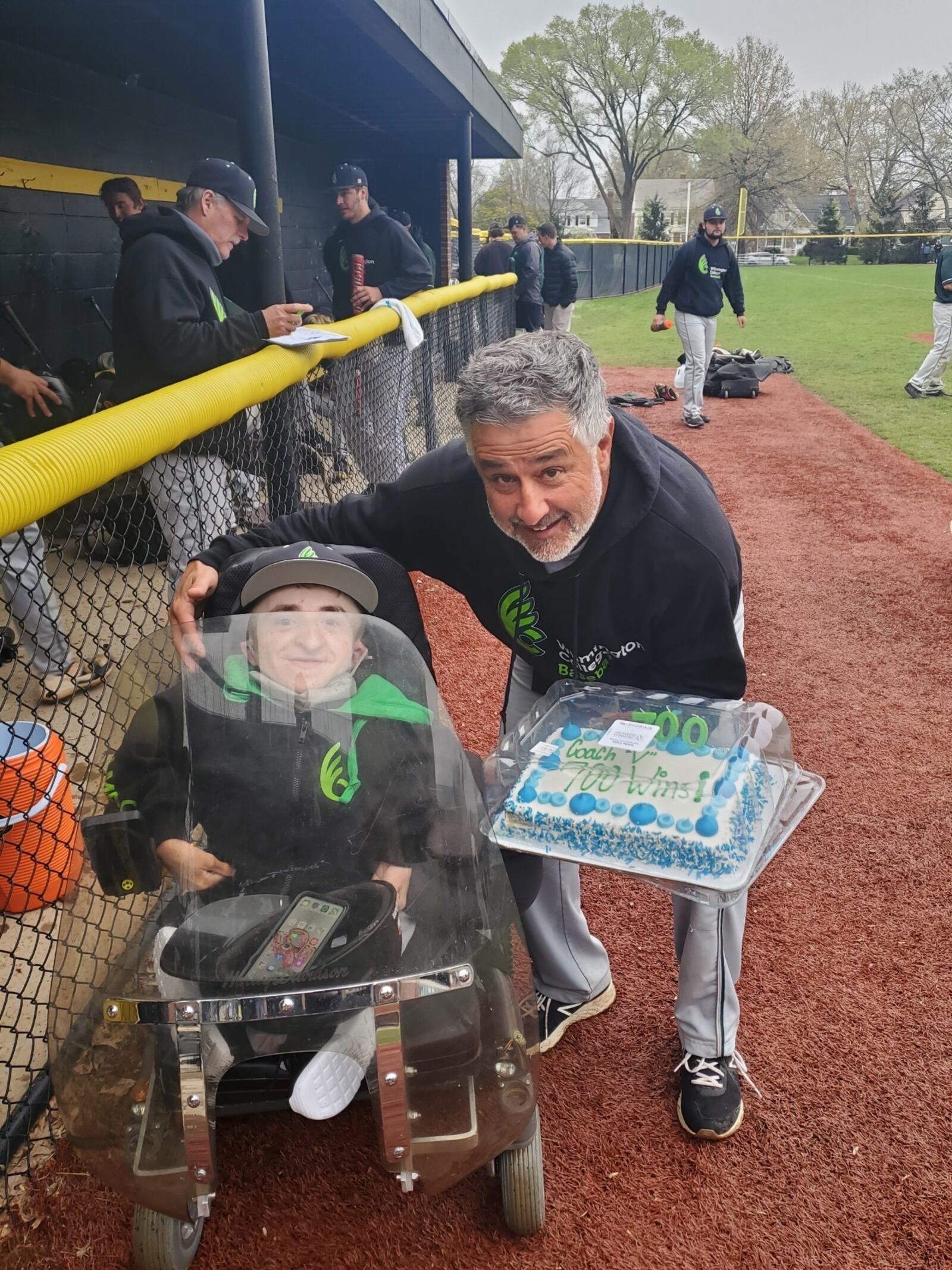 Wilmington coach Tony Vittorio celebrates his 700th win as  college baseball coach with Fightin Quakers assistant coach Daniel “Danny” McCarty, who moves around the field in a motorized wheelchair that he has equipped with a Harley Davidson motorcycle shield to protect his brittle bones from hits or errantly thrown baseballs at games. McCarty said he has suffered over 300 broken bones in his 18 years of life (Contributed Photo)