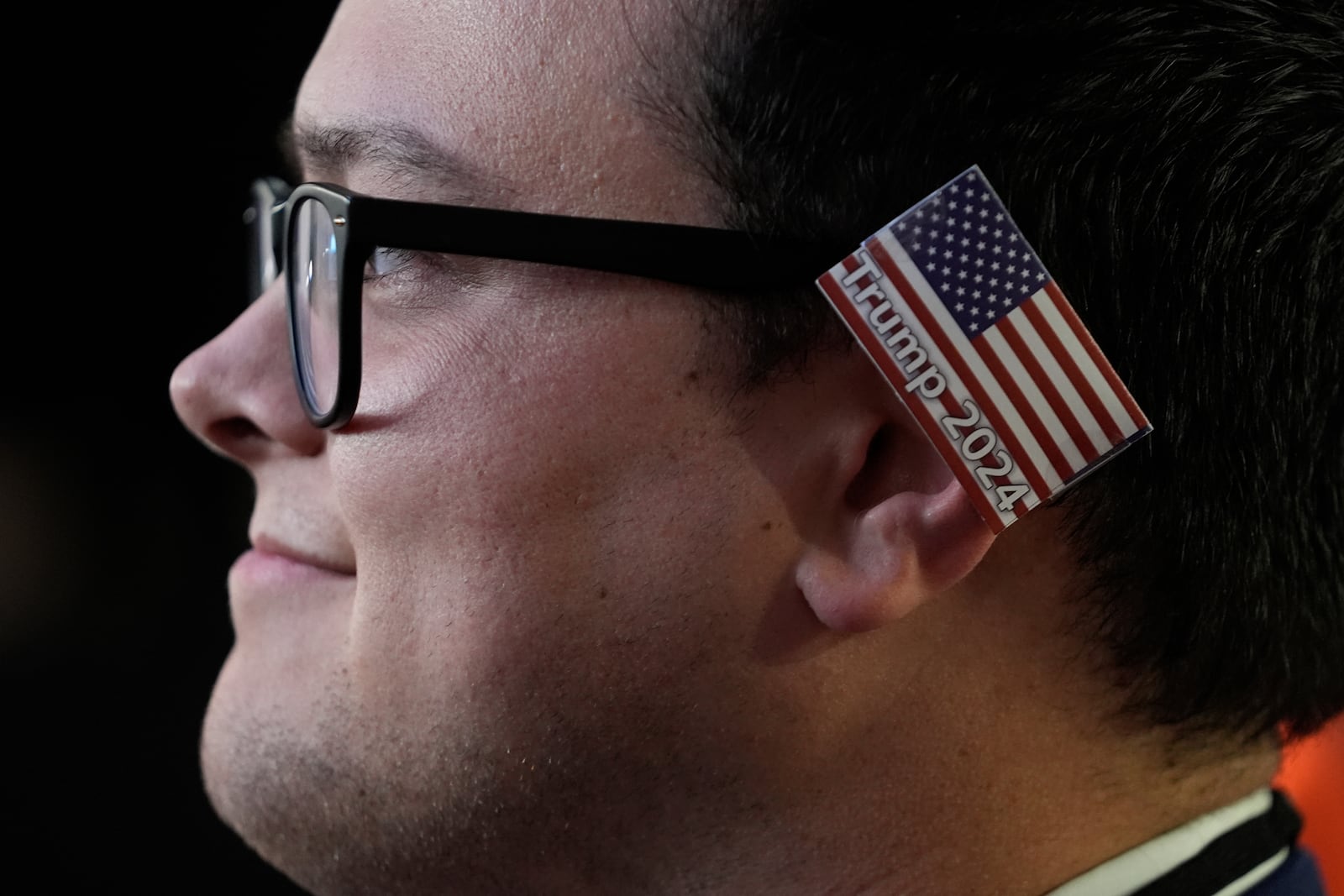 A delegate wearing a small American flag on his ear watches as Republican presidential candidate and former president, Donald Trump, speaks during the final day of the Republican National Convention Thursday, July 18, 2024, in Milwaukee. (AP Photo/Paul Sancya)