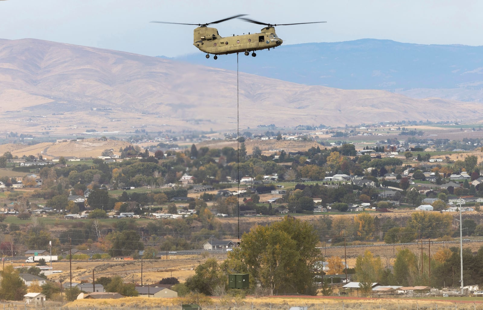 A U.S. Army Chinook helicopter lifts a cargo box out of Vagabond Army Heliport as it heads toward the site of the crashed Navy EA-18G Growler jet on Friday, Oct. 18, 2024, in Yakima, Wash. (Nick Wagner/The Seattle Times via AP)