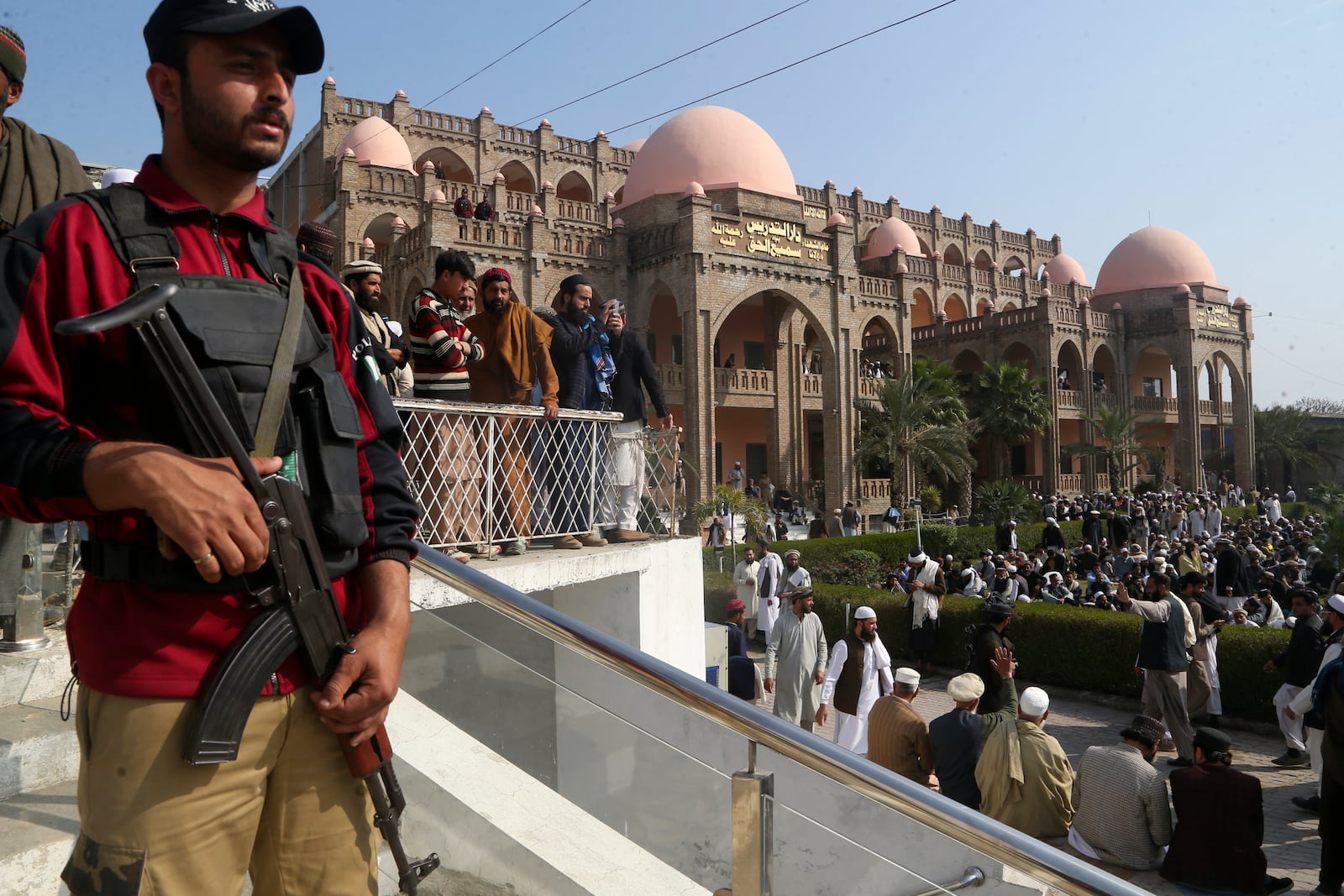 A police officer stands guard as mourners arrive to attend the funeral prayer of a senior Muslim cleric, Hamidul Haq who was killed in the Friday's suicide bomb attack, at a pro-Taliban seminary in Akora Khattak, Pakistan, Saturday, March 1, 2025. (AP Photo/Muhammad Sajjad)