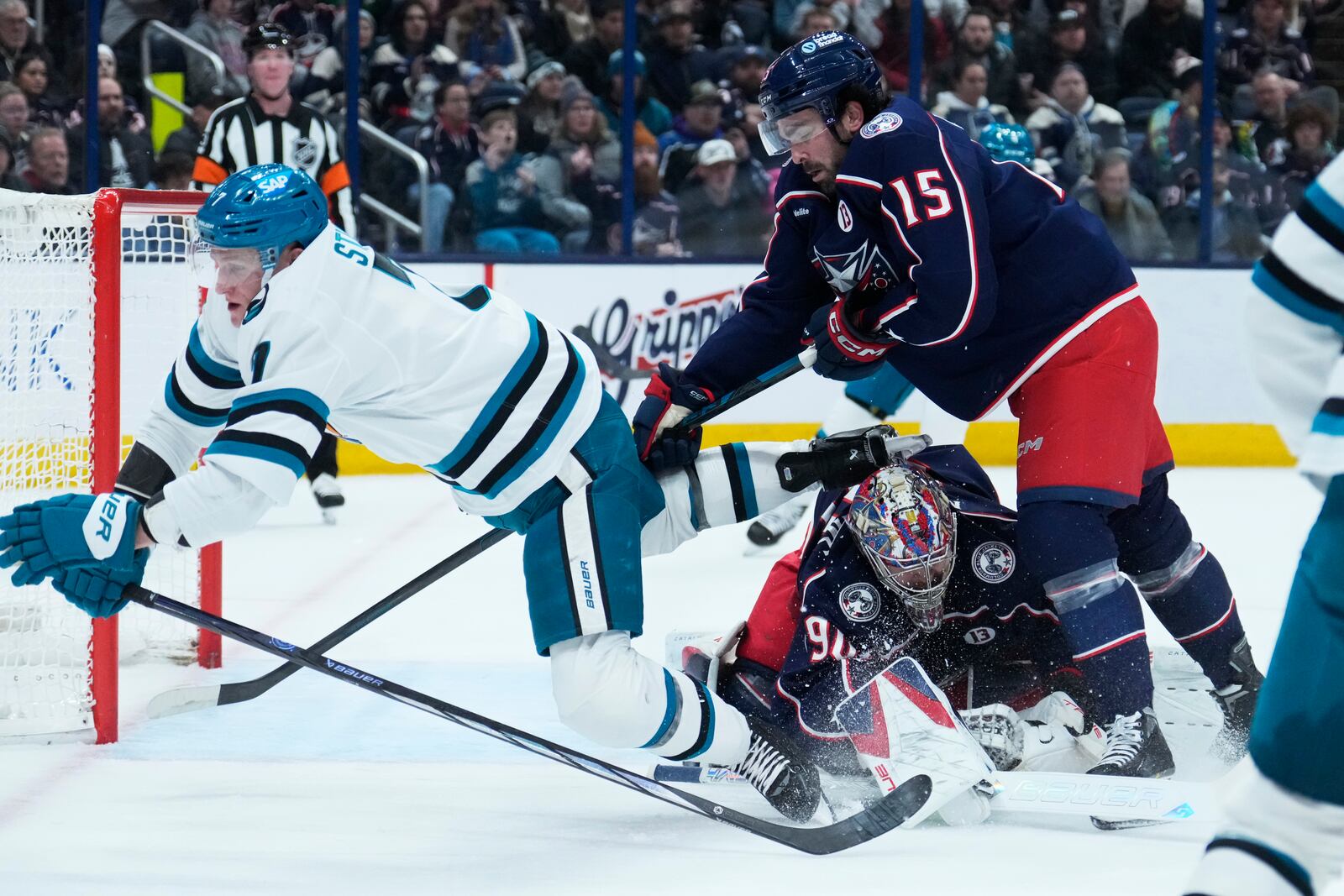 San Jose Sharks center Nico Sturm (7) trips over Columbus Blue Jackets goaltender Elvis Merzlikins (90) in front of defenseman Dante Fabbro (15) in the first period of an NHL hockey game Thursday, Jan. 16, 2025, in Columbus, Ohio. (AP Photo/Sue Ogrocki)