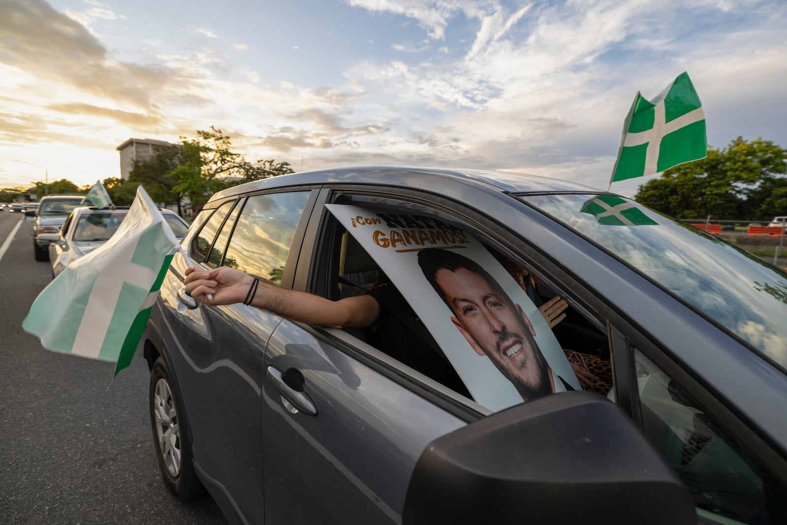 A supporter waves a Puerto Rican Independence Party flag while holding a campaign poster promoting the Citizens' Victory Movement mayoral candidate Manuel Natal, during a caravan in San Juan, Puerto Rico, Friday, Nov. 1, 2024. (AP Photo/Alejandro Granadillo)