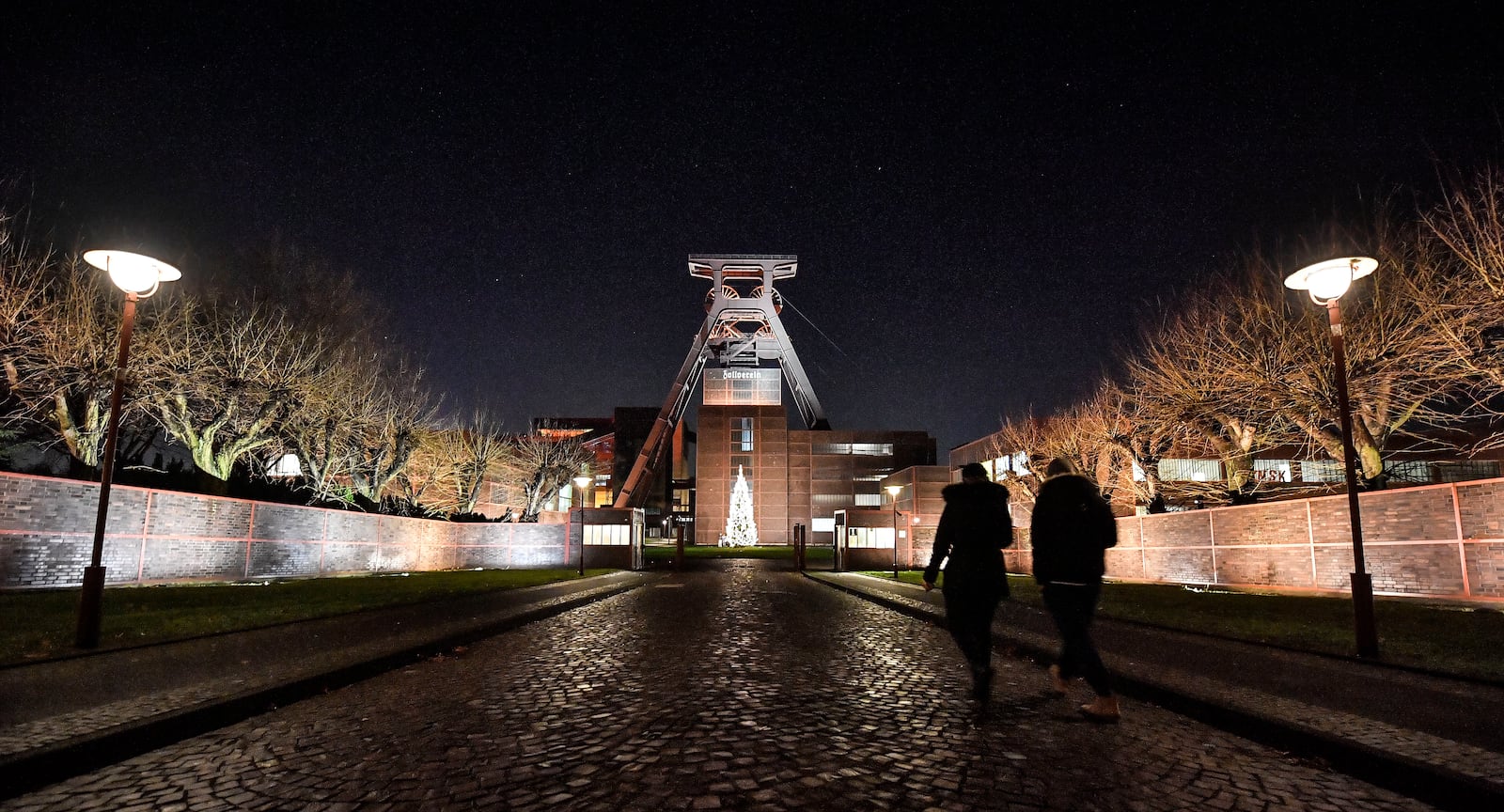 FILE - People walk to the illuminated Bauhaus coal mine complex and UNESCO World Heritage Site Zollverein in Essen, Germany, Monday, Dec. 17, 2018. (AP Photo/Martin Meissner, File)