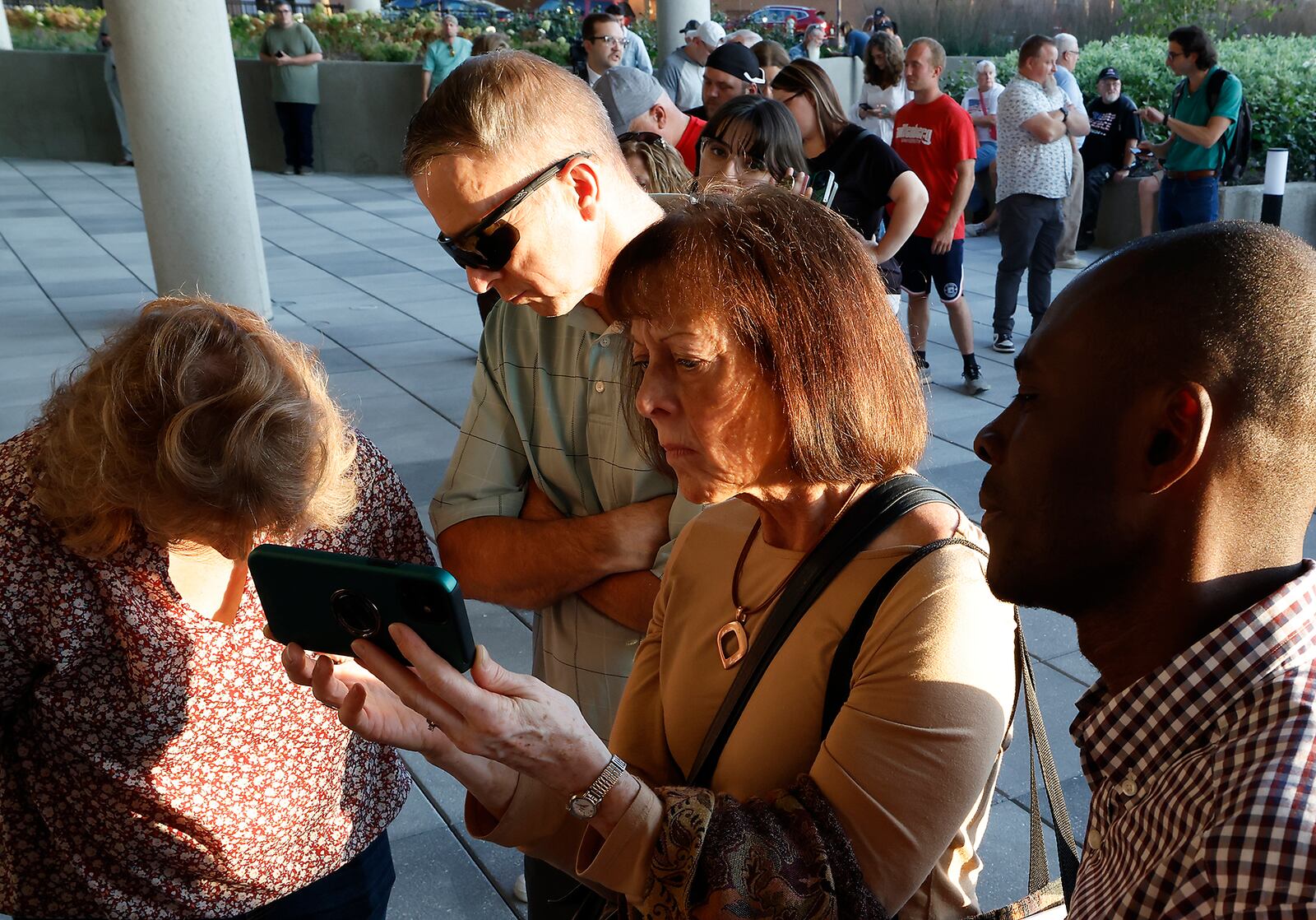 A group of concerned citizens, unable to get into the Springfield City Commission meeting due to capacity being reached, crowd around a cell phone as they watch and listen to the meeting on the City Hall Plaza on Tuesday, Sept. 10, 2024. BILL LACKEY/STAFF