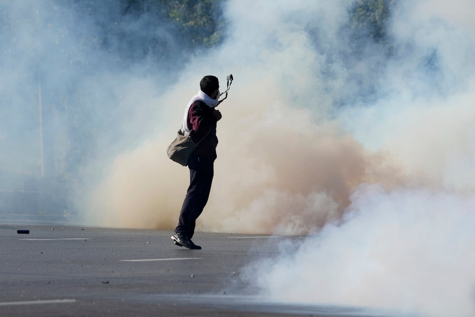 A police officer aims to throw stone with a slingshot after others fire tear gas shells to disperse supporters of imprisoned former Premier Imran Khan's Pakistan Tehreek-e-Insaf party, during clashes in Islamabad, Pakistan, Tuesday, Nov. 26, 2024. (AP Photo/Anjum Naveed)