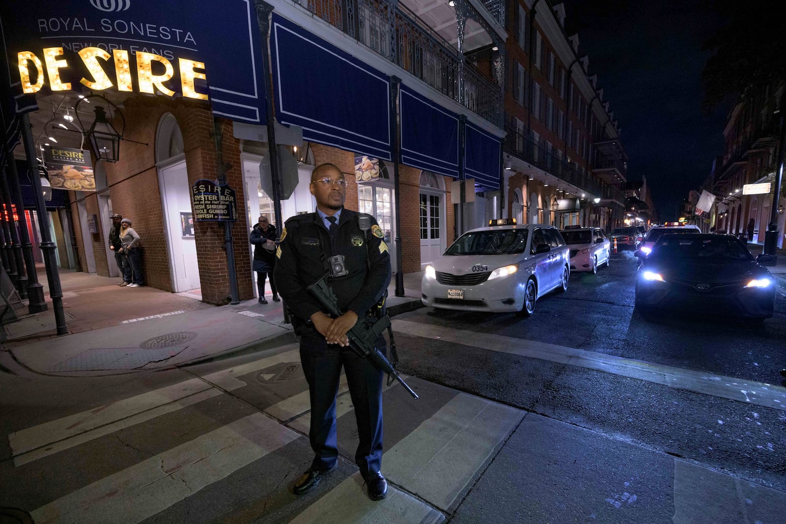 A New Orleans Police officer carries an assault rifle as he stands guard on Bourbon Street during a parade memorializing the victims of the New Year's Day deadly truck attack and shooting in New Orleans, Saturday, Jan. 4, 2025. (AP Photo/Matthew Hinton)