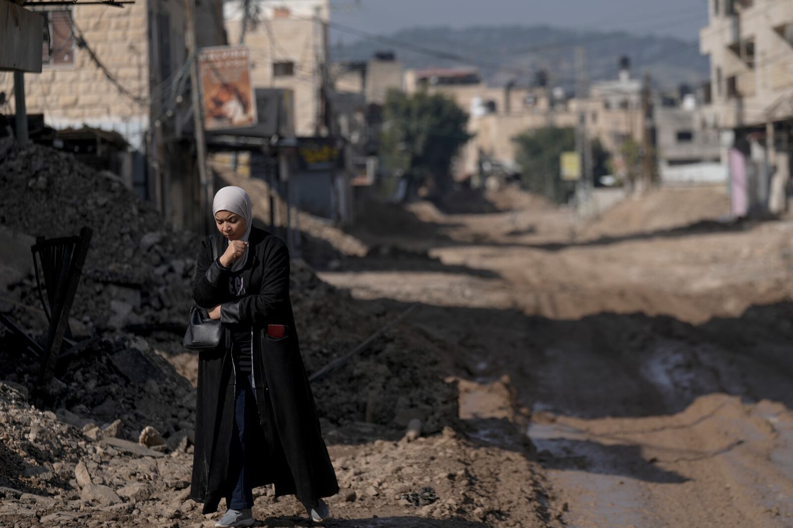 A Palestinian woman walks along a destroyed road following an Israeli army raid in the West Bank Jenin refugee camp, Sunday, Feb. 2, 2025. (AP Photo/Majdi Mohammed)