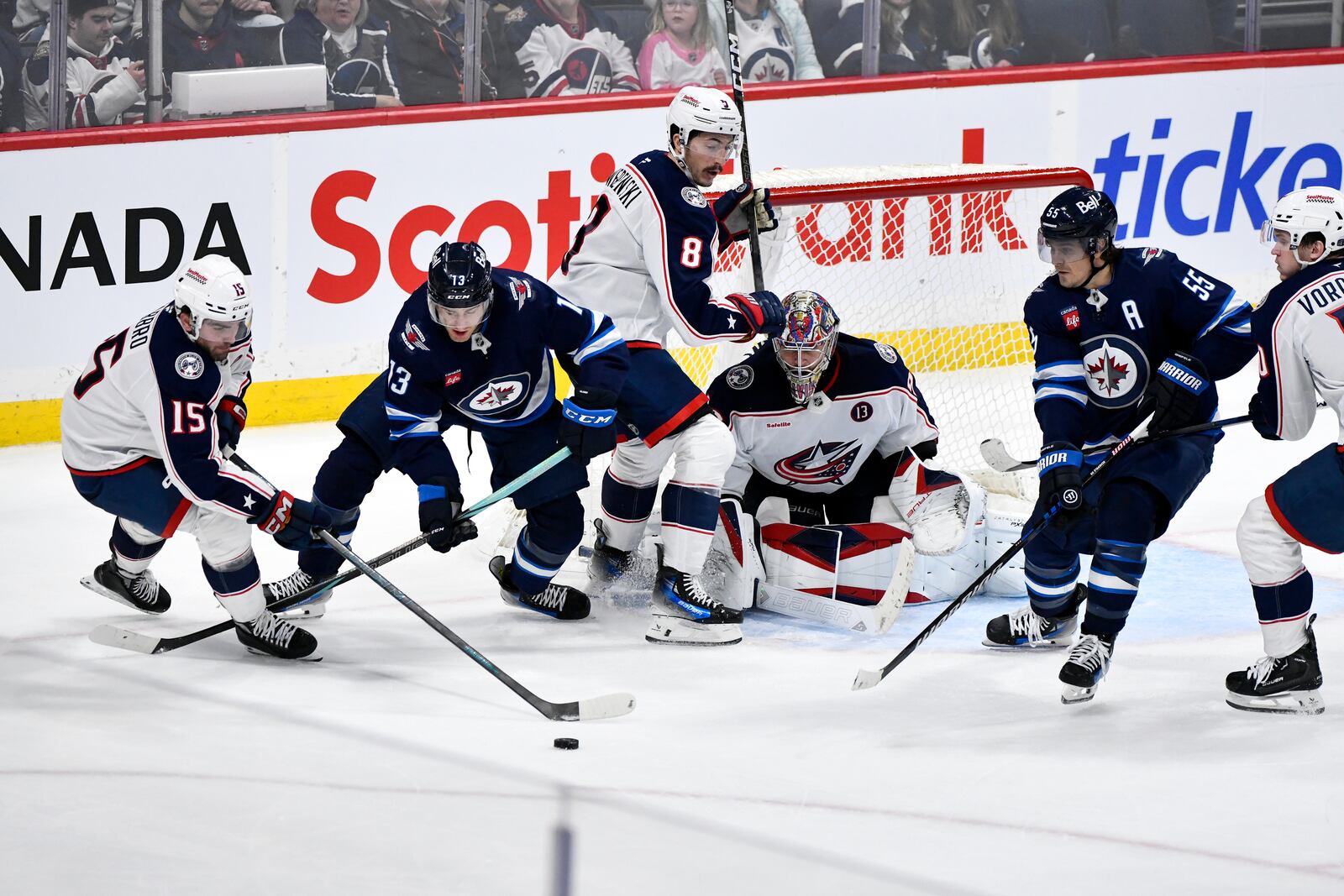 Columbus Blue Jackets' Dante Fabbro (15) carries the puck up ice past Winnipeg Jets' Gabriel Vilardi (13) and Mark Scheifele (55) as Zach Werenski (8) defends in front of goaltender Elvis Merzlikins (90) during the third period of an NHL hockey game in Winnipeg, Manitoba, Sunday, Dec. 8, 2024. (Fred Greenslade/The Canadian Press via AP)