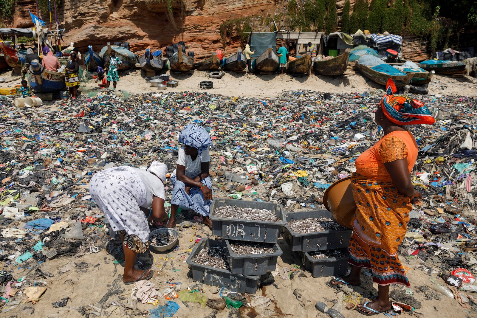 Women sort fish through textile waste on the beach shore at Jamestown in Accra, Ghana, Saturday, Oct. 19, 2024. (AP Photo/Misper Apawu)