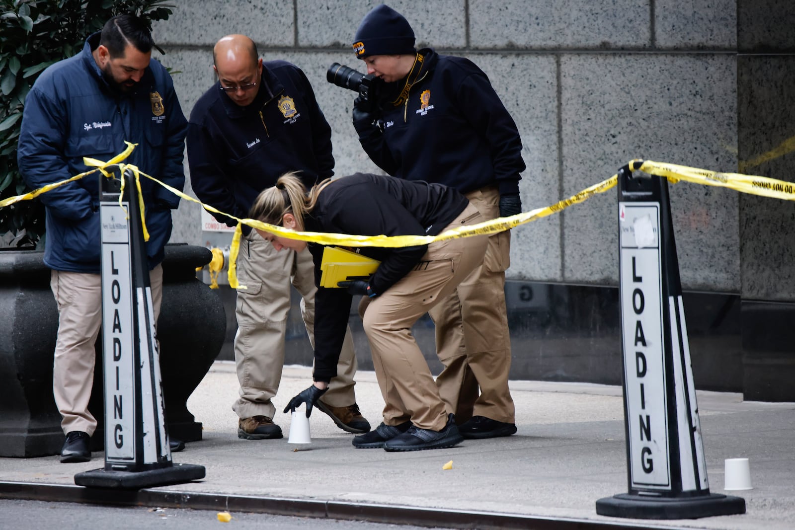 Members of the New York police crime scene unit pick up cups marking the spots where bullets lie as they investigate the scene outside the Hilton Hotel in midtown Manhattan where Brian Thompson, the CEO of UnitedHealthcare, was fatally shot Wednesday, Wednesday, Dec. 4, 2024, in New York. (AP Photo/Stefan Jeremiah)