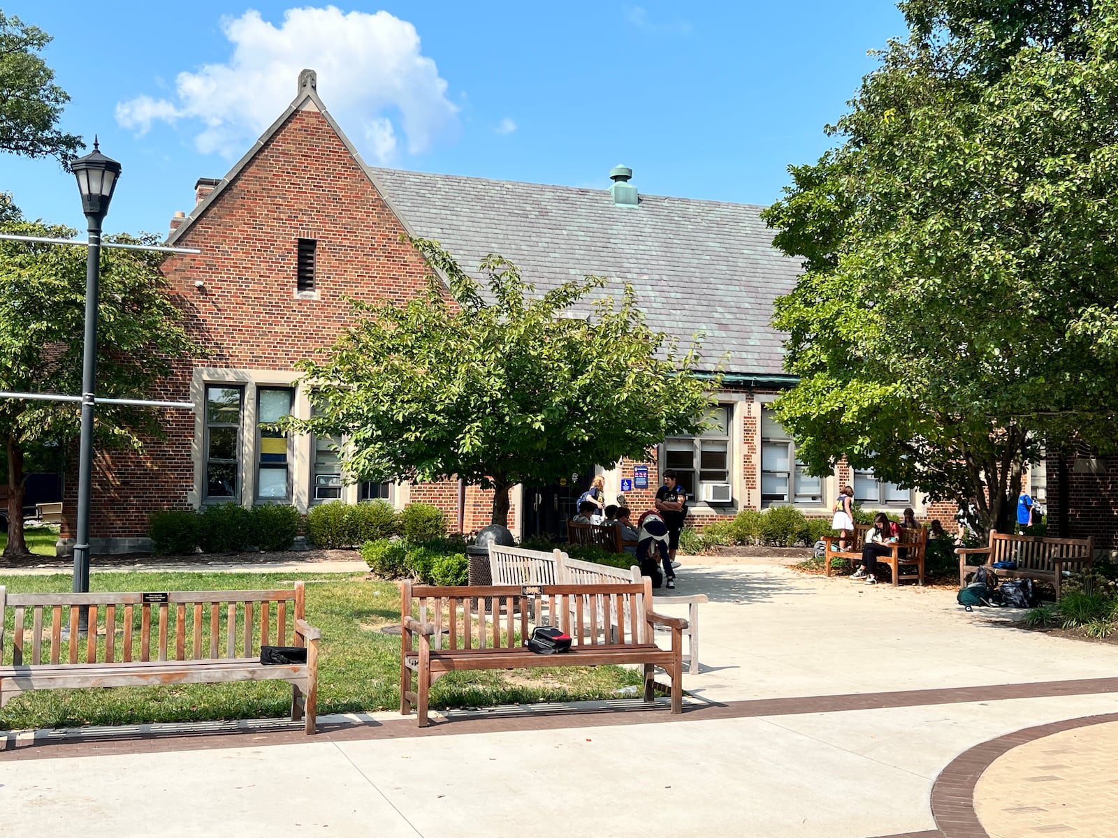 Students exit the exterior of Oakwood Junior High, a brick building, along a sidewalk lined with trees and benches.