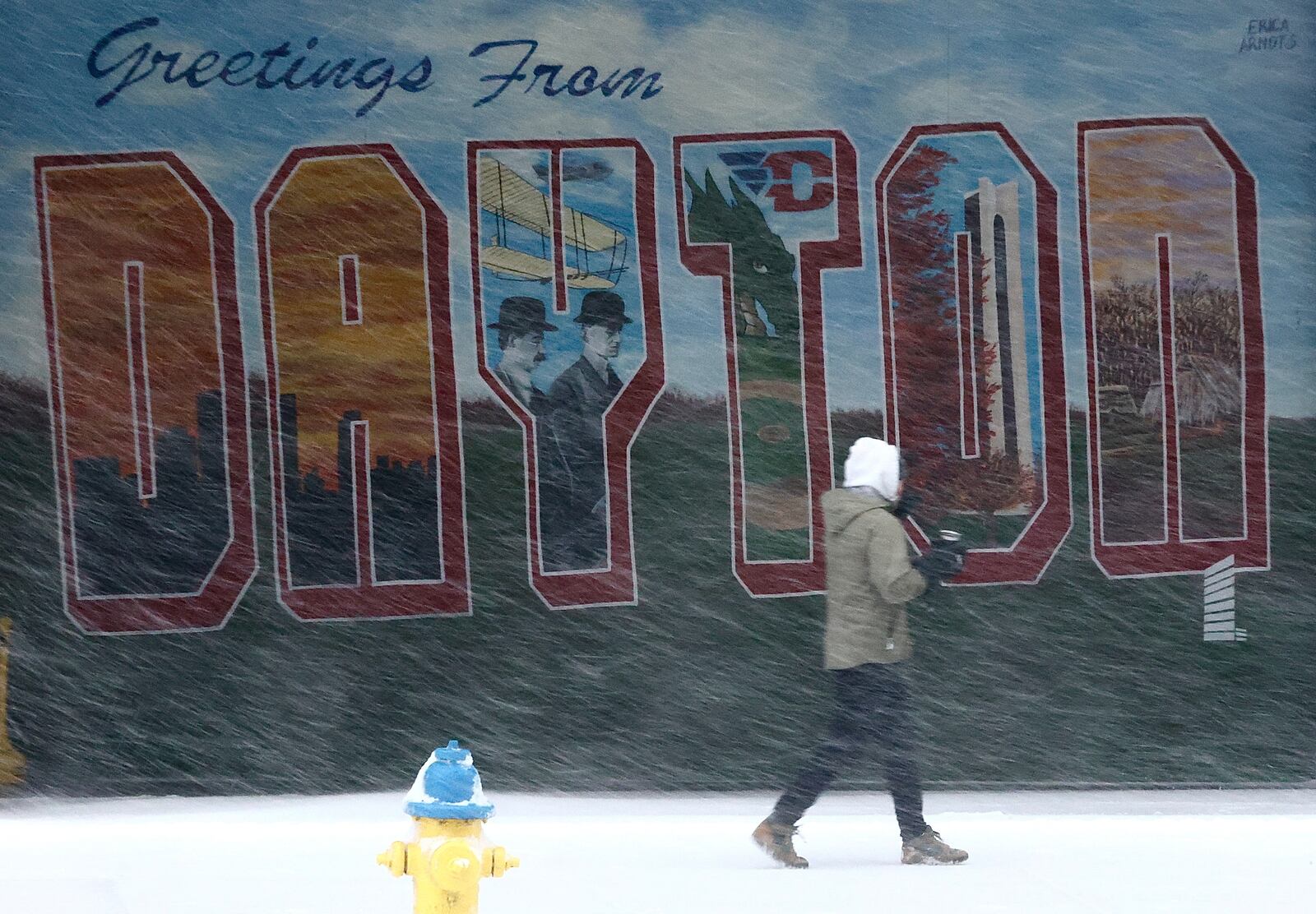 A woman walks past a mural in the blowing snow Thursday evening.