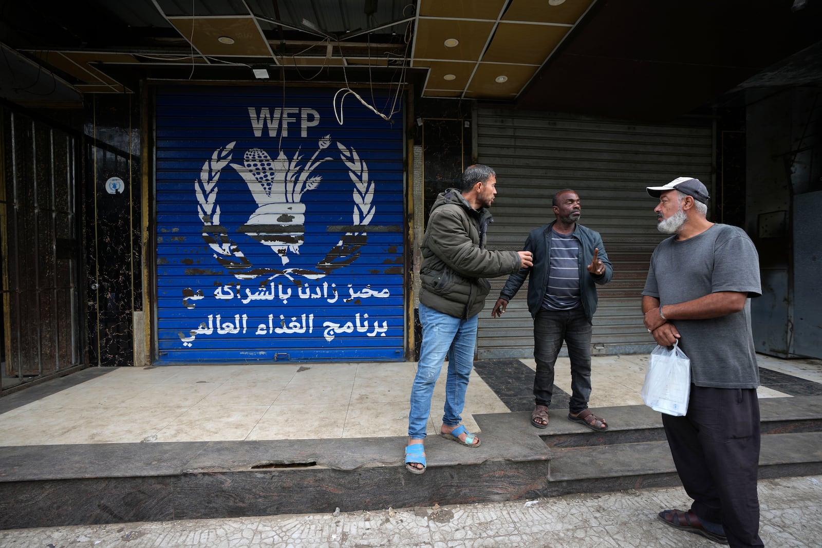 Palestinians gather near a closed bakery, amid a shortage in flour and the closure of a main bakery in central Gaza have exacerbated an already dire humanitarian situation, in Deir al-Balah, Gaza Strip, Monday, Nov. 18, 2024. (AP Photo/Abdel Kareem Hana)