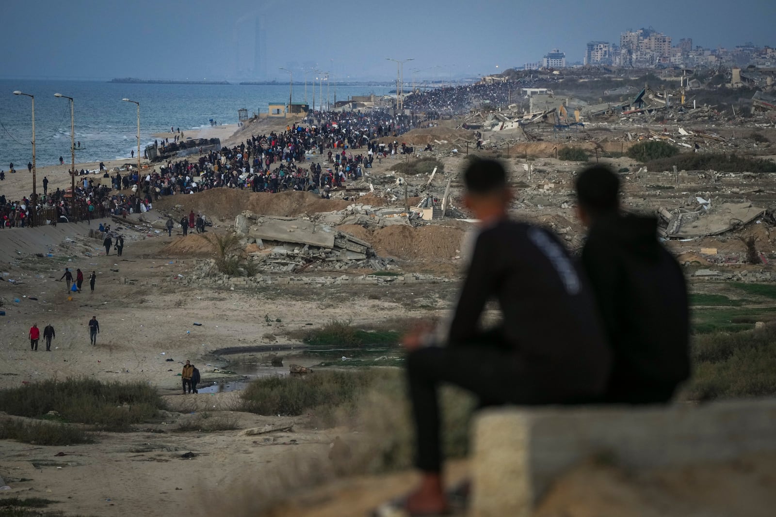 Two boys watch a crowd of Palestinians returning to northern Gaza, amid destroyed buildings, following Israel's decision to allow thousands of them to return for the first time since the early weeks of the 15-month war with Hamas, Monday, Jan. 27, 2025. (AP Photo/Abdel Kareem Hana)