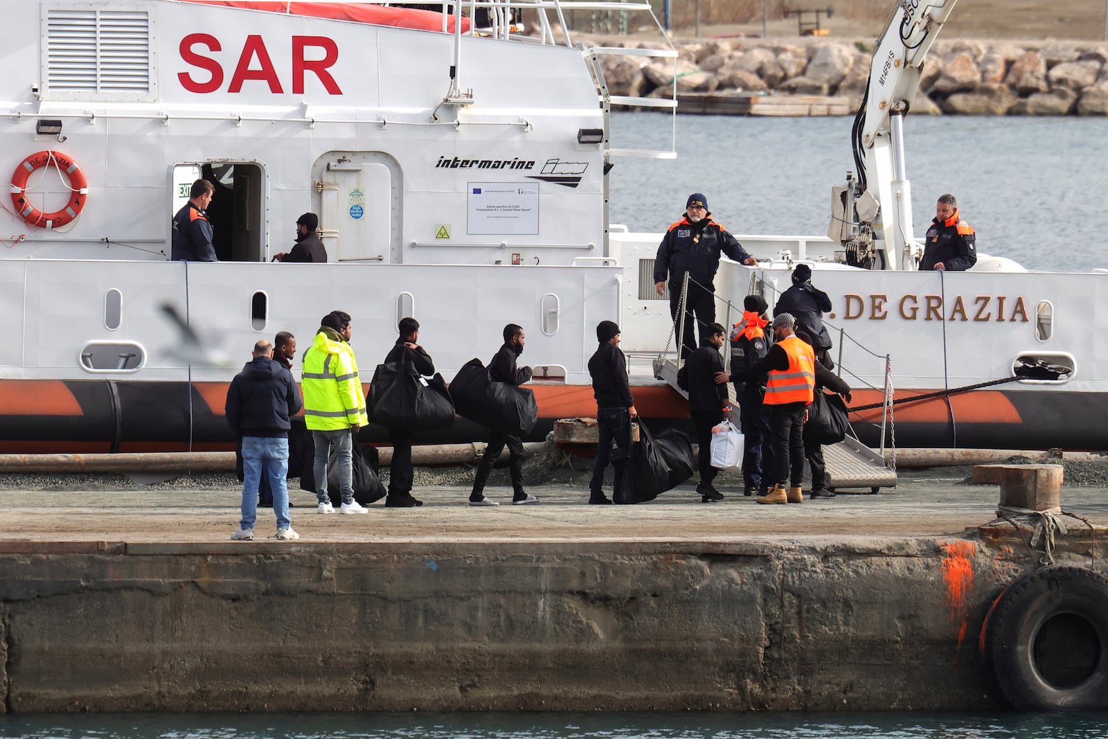 Migrants board an Italian Coast Guard vessel as part of a transfer operation from the asylum processing centers in Albania back to Italy following a court decision in Rome, at the port of Shengjin, northwestern Albania, Saturday, Feb. 1, 2025. (AP Photo/Vlasov Sulaj)