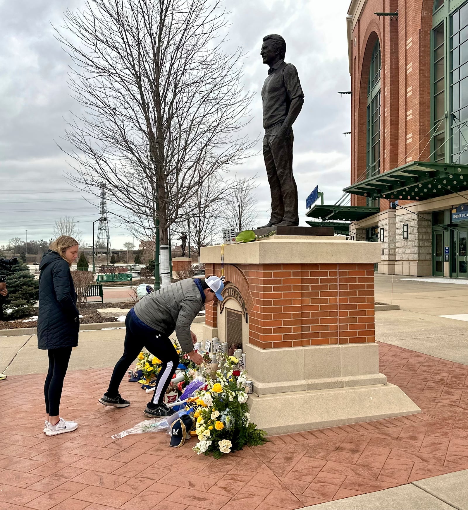 E.J. Kuster, right, of Milwaukee, lays flowers at the base of a statue honoring Bob Uecker outside American Family Field in Milwaukee as Deanna White. left, looks on Thursday, Jan. 16, 2025. (AP Photo/Steve Megargee)