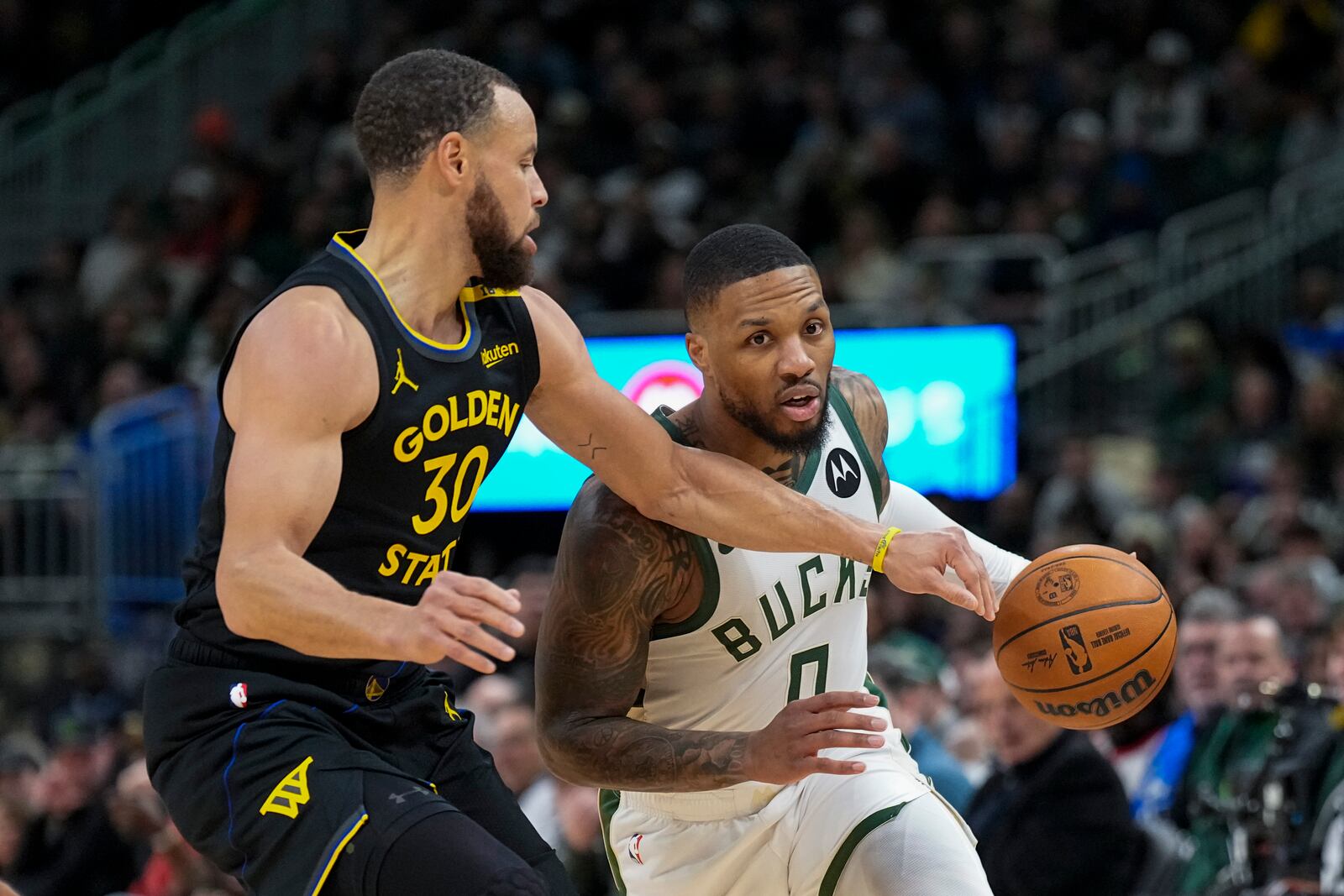 Milwaukee Bucks' Damian Lillard (0) controls the ball against against Golden State Warriors' Stephen Curry (30) during the first half of an NBA basketball game Monday, Feb. 10, 2025, in Milwaukee. (AP Photo/Andy Manis)