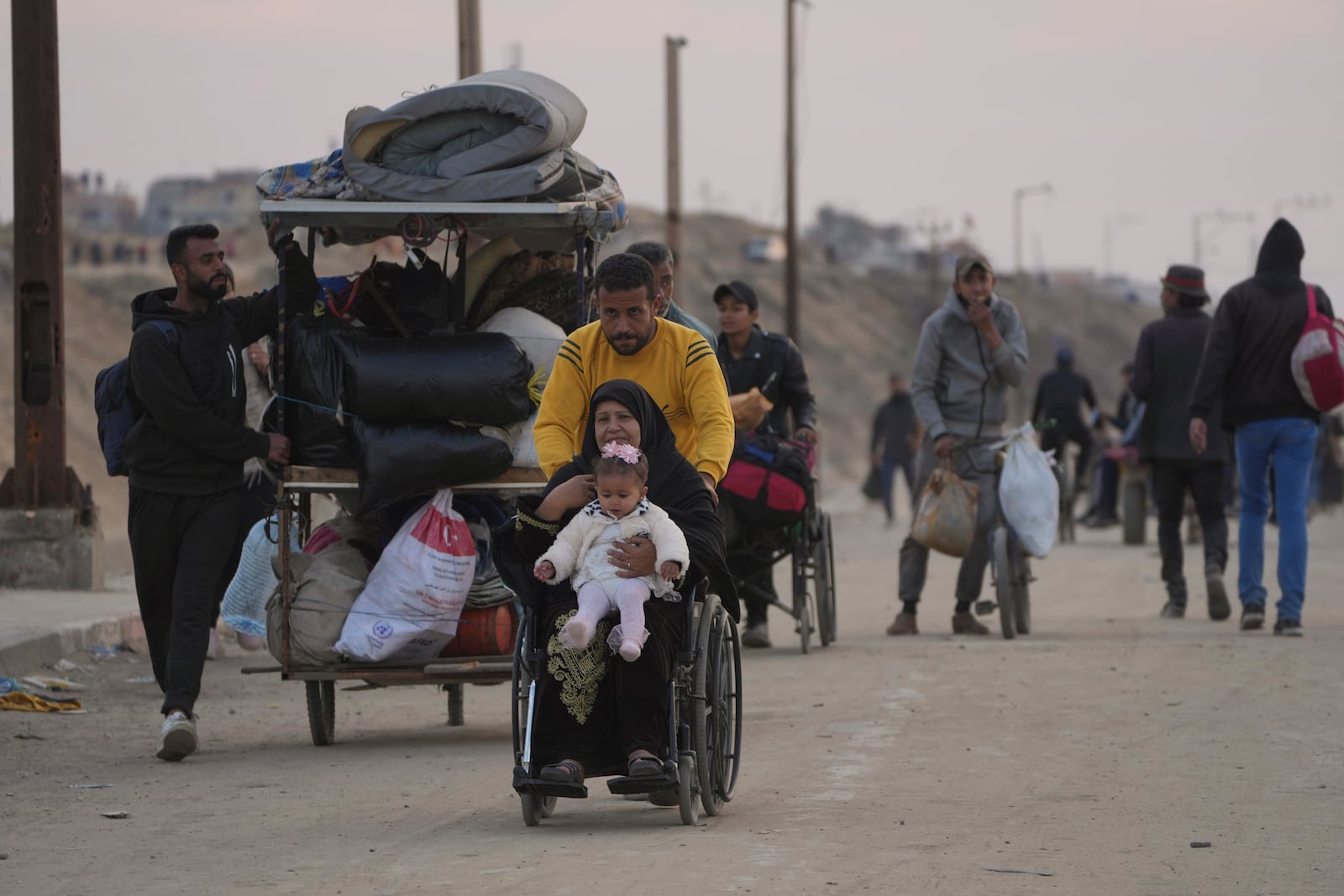 A displaced Palestinian pushes a woman in a wheelchair holding a baby on a road to return to their homes in the northern Gaza Strip, Tuesday, Jan. 28, 2025. (AP Photo/Abdel Kareem Hana)