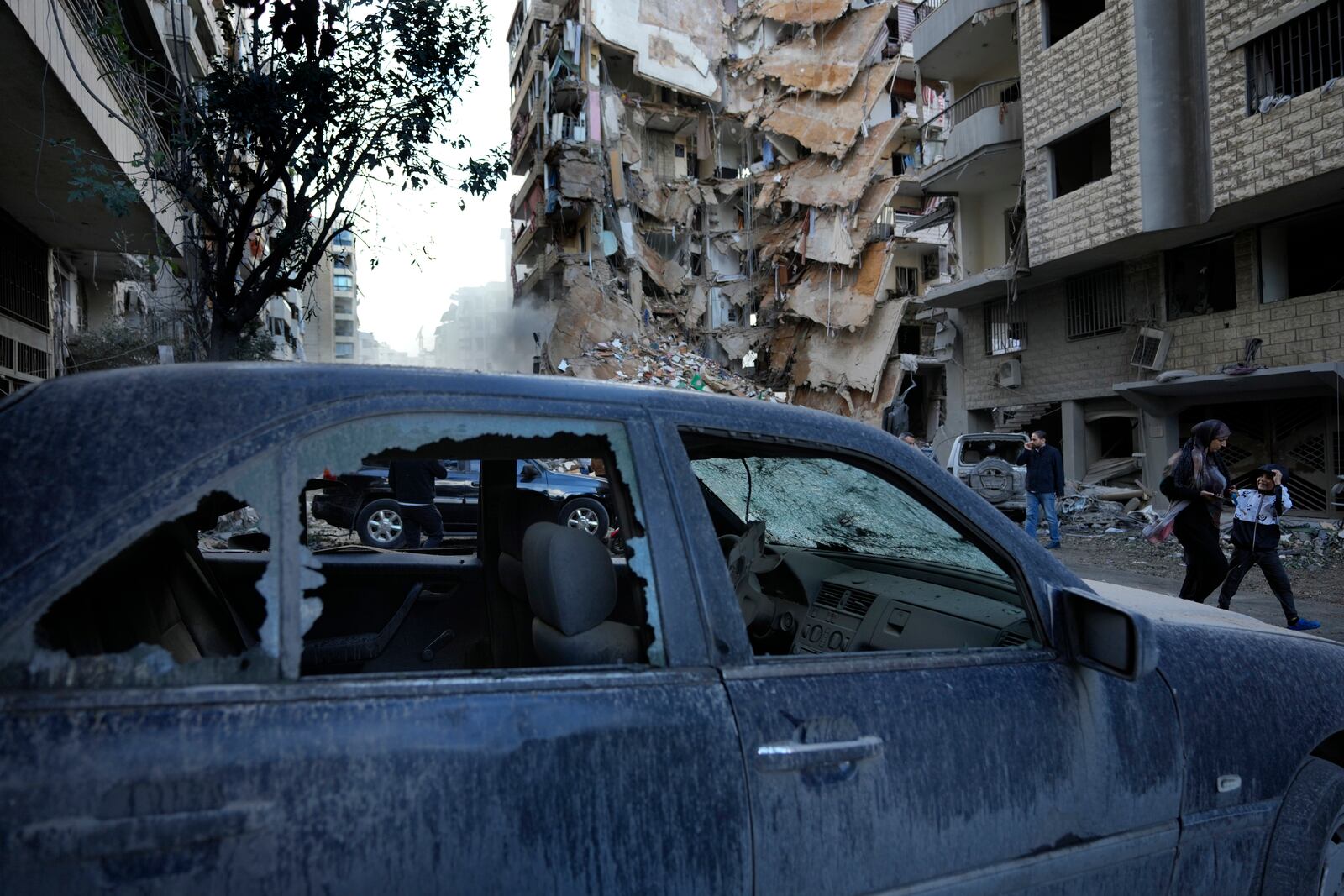 Residents pass in front of a destroyed building that was hit Sunday night in an Israeli airstrike in Dahiyeh, in the southern suburb of Beirut, Lebanon, Monday, Nov. 25, 2024. (AP Photo/Hussein Malla)