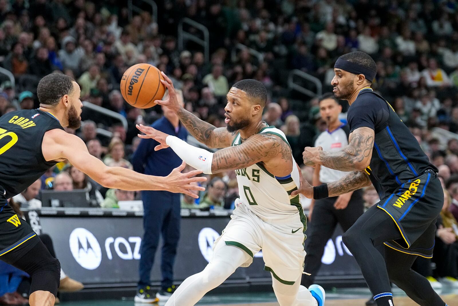 Milwaukee Bucks' Damian Lillard (0) looks to pass thee ball against Golden State Warriors' Stephen Curry, left, during the first half of an NBA basketball game Monday, Feb. 10, 2025, in Milwaukee. (AP Photo/Andy Manis)