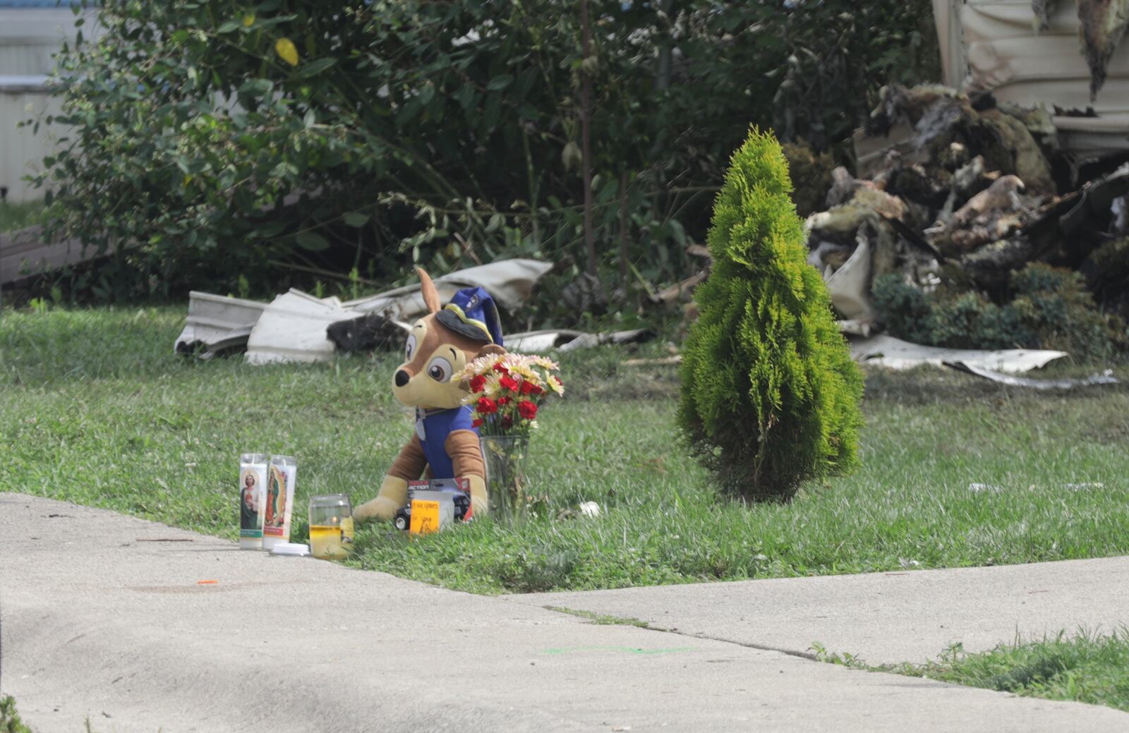 A stuffed police dog sits with a small memorial in front of the burned out mobile home at Harmony Estates Monday morning. BILL LACKEY/STAFF