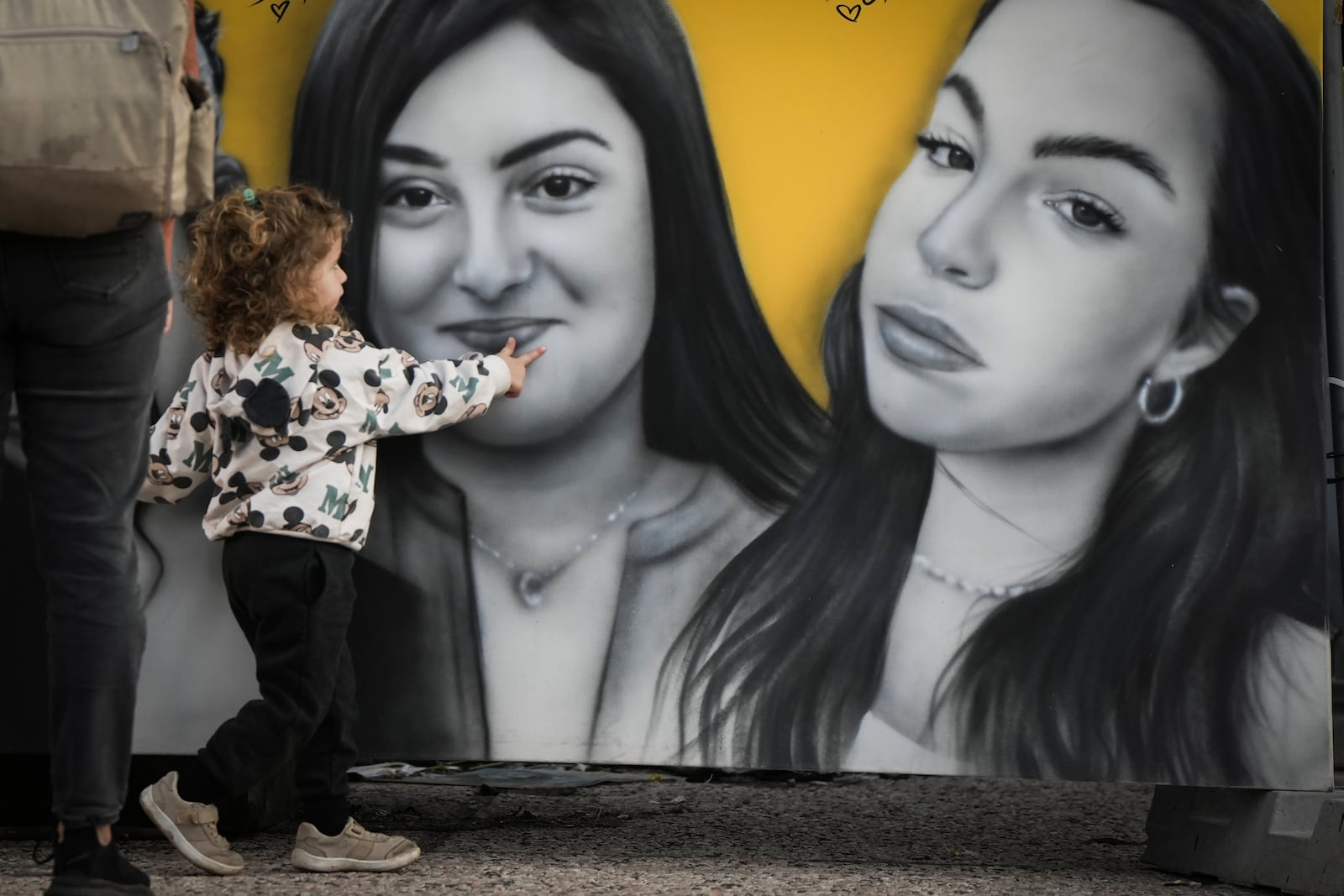 A little girl touches a mural showing female Israeli soldiers taken hostage during the Oct. 7, 2023 Hamas-led attack on Israel in Tel Aviv, Israel, Saturday Jan. 18, 2025.(AP Photo/Oded Balilty)