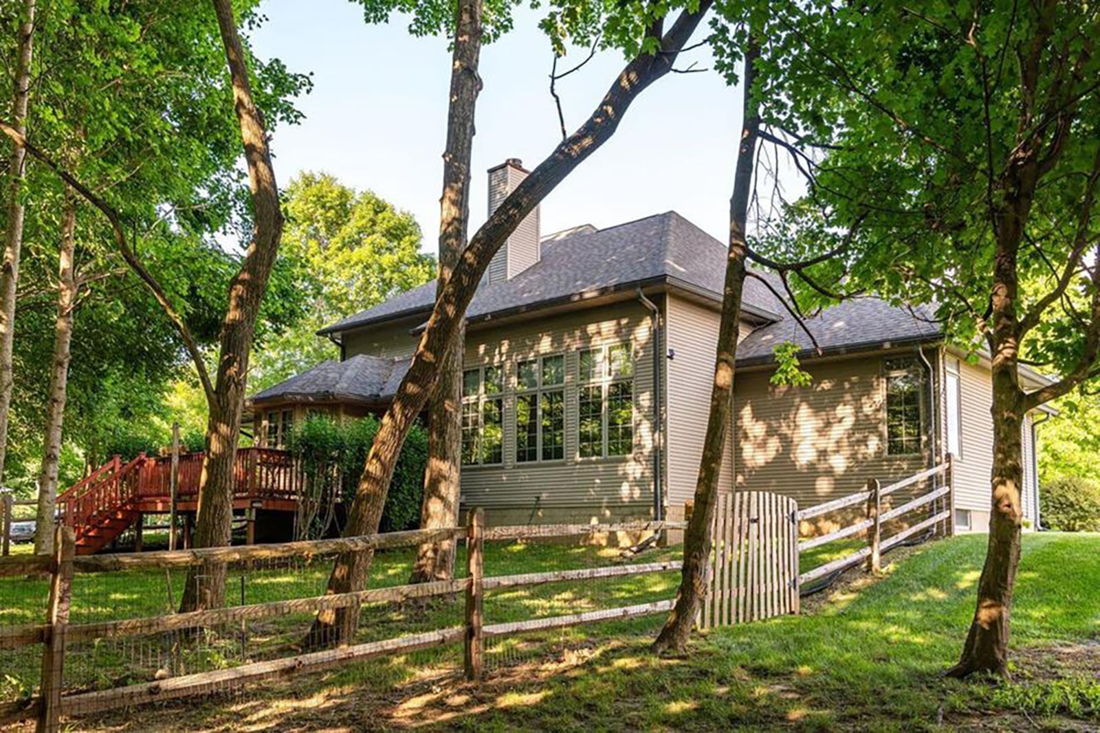 The rear of the home is mostly wooded and features a wood raised deck with railings and a wood fence.