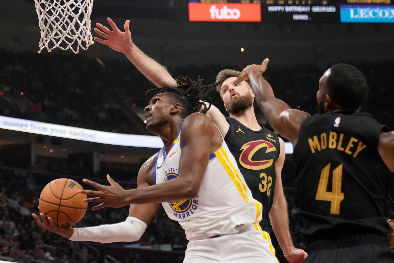 Golden State Warriors forward Kevon Looney, left, goes to the basket in front of Cleveland Cavaliers forward Dean Wade (32) and forward Evan Mobley (4) in the first half of an NBA basketball game, Friday, Nov. 8, 2024, in Cleveland. (AP Photo/Sue Ogrocki)