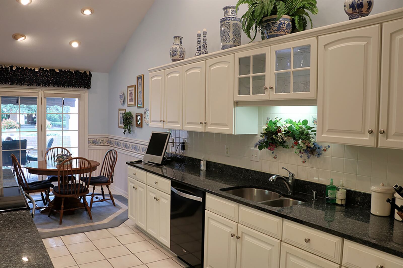 A galley-style kitchen has white cabinetry with dark granite countertops and black appliances. White ceramic-tile backsplash matches the white ceramic-tile flooring. Wainscoting accents the walls of the breakfast room, which has sliding patio doors that open out to the paver-brick, courtyard patio that has a retractable awning. CONTRIBUTED PHOTO BY KATHY TYLER