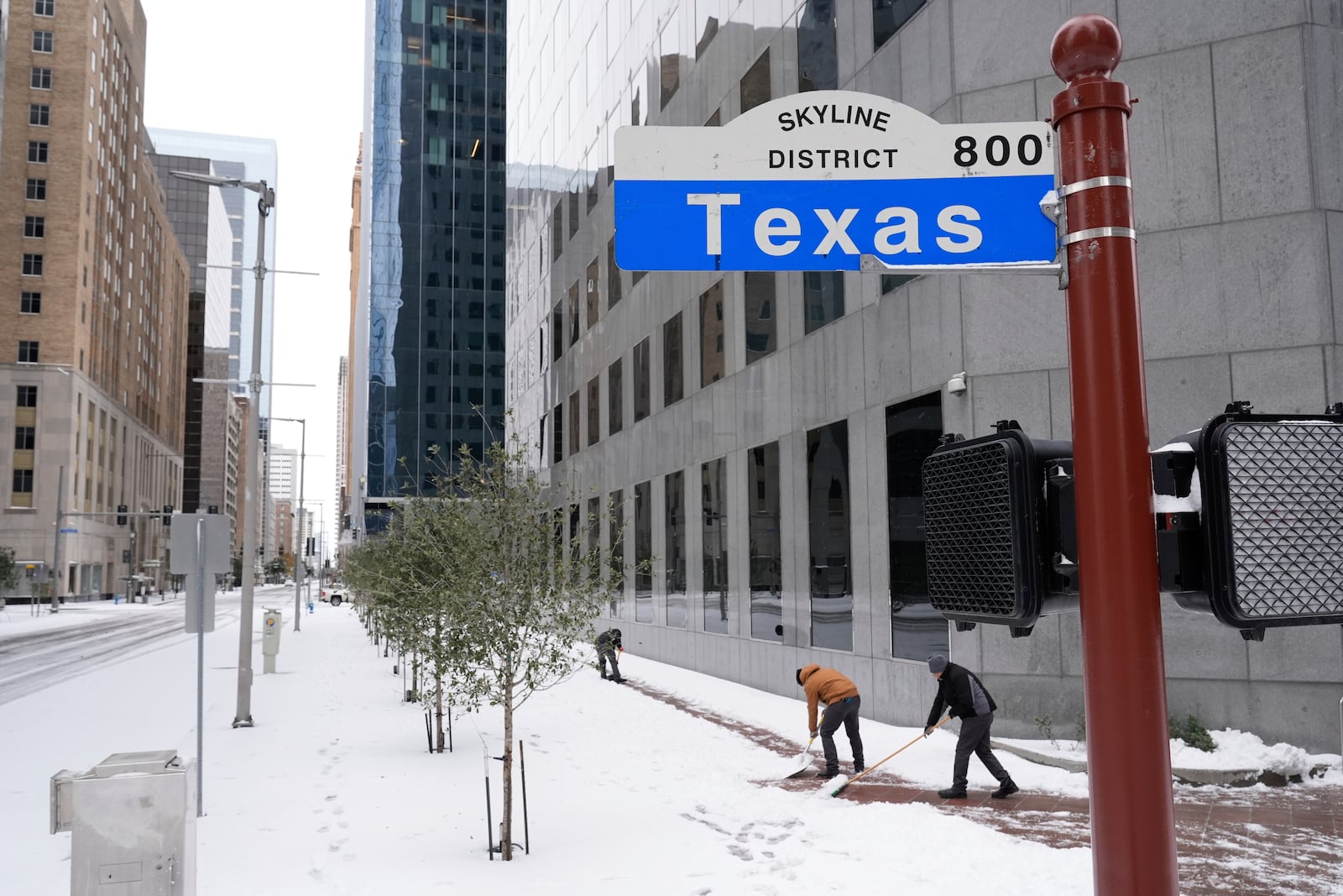 People shovel snow off the sidewalk Tuesday, Jan. 21, 2025, in downtown Houston. (AP Photo/Ashley Landis)