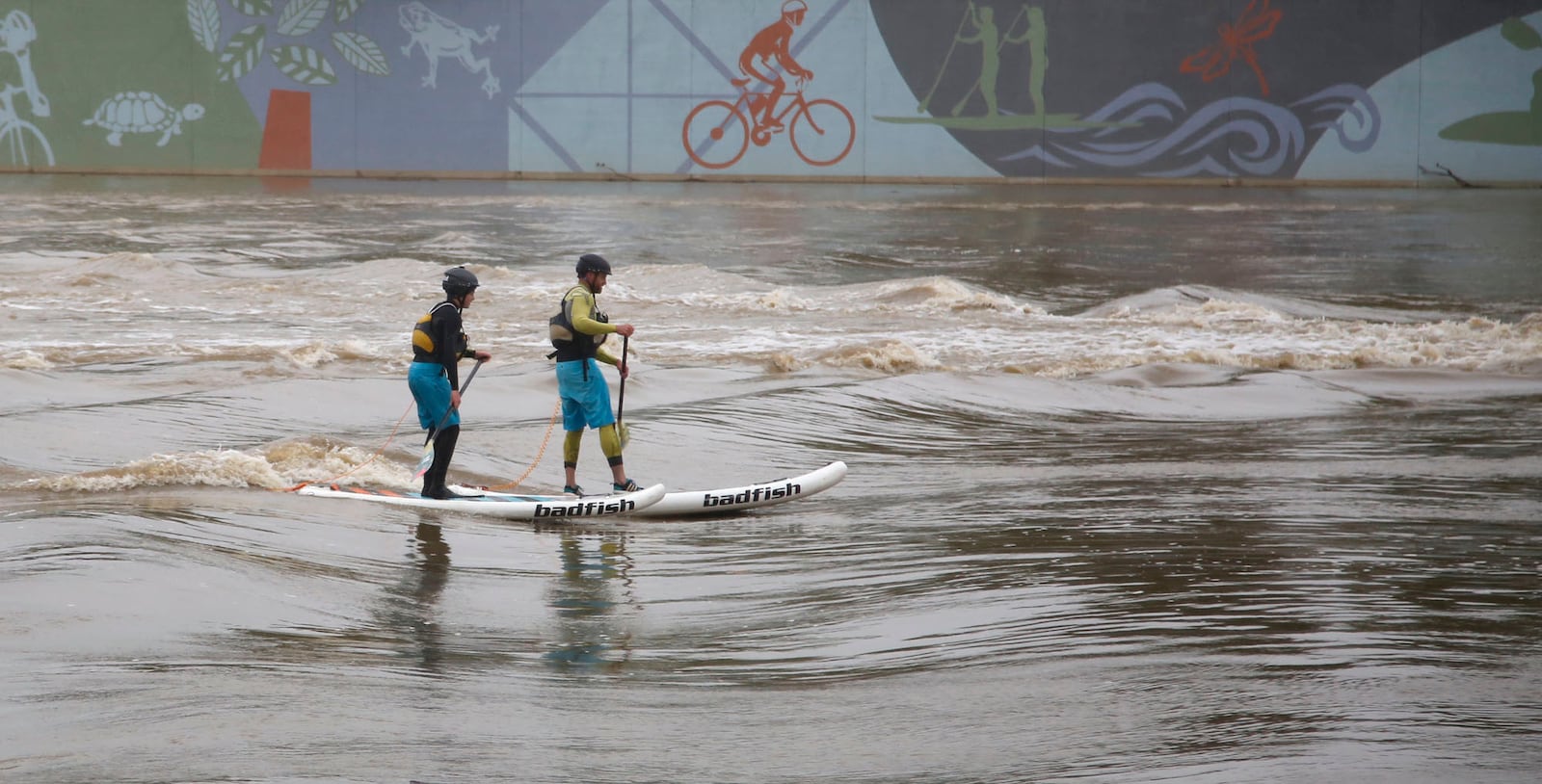 Riverscape River Run was officially opened on Friday with a ribbon cutting by the Downtown Dayton Partnership.  River Run designer Mike Harvey, right,  and his son Miles Harvey floated stand-up paddle boards on the rain swollen Great Miami River to show off the new River Run Features.     TY GREENLEES / STAFF