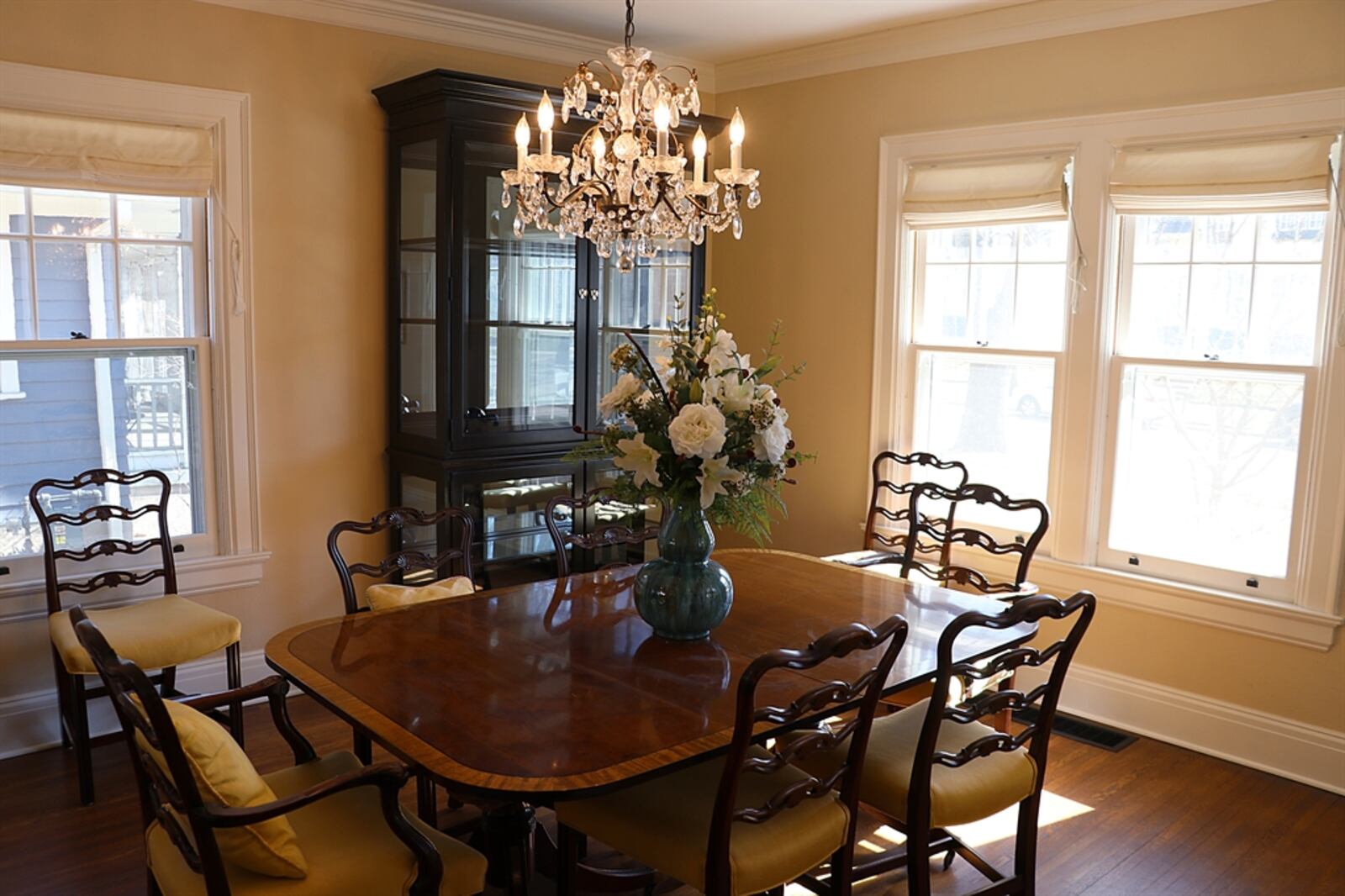 The formal dining room has three sets of windows and crown molding that frames the crystal chandelier. French doors with custom shades and screen doors open out to the same front porch.