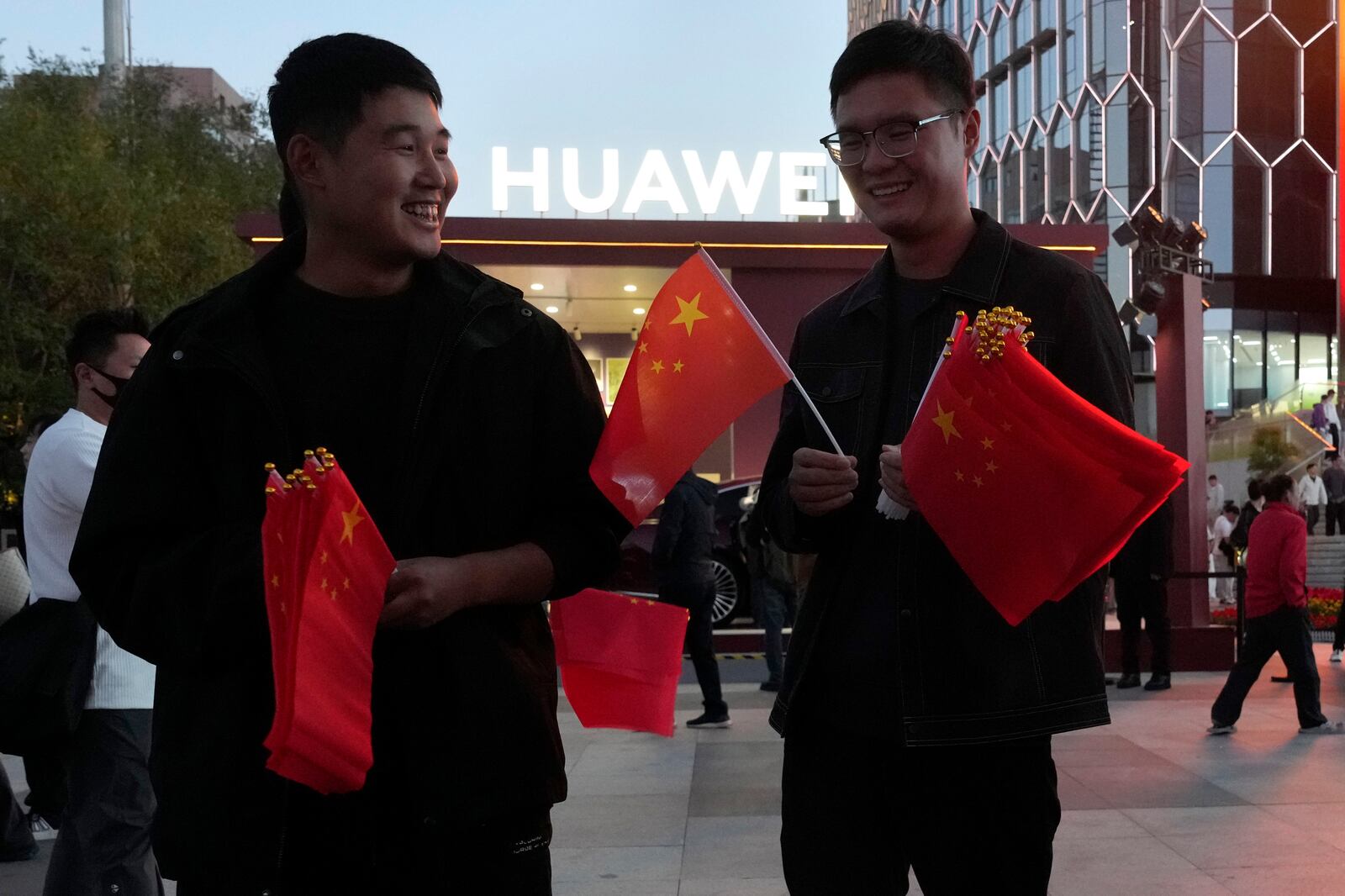 FILE - Chinese men hand out national flags during national day holidays near a Huawei pop up store in Beijing, Oct. 2, 2024. (AP Photo/Ng Han Guan, File)