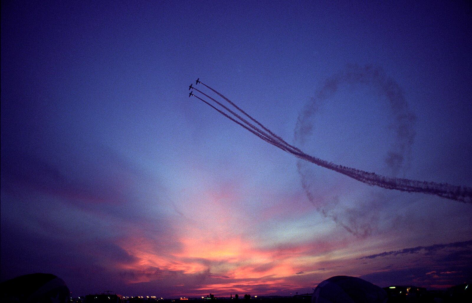 A formation of three WWII era T-6 Texans loops through a painting-like sunset.