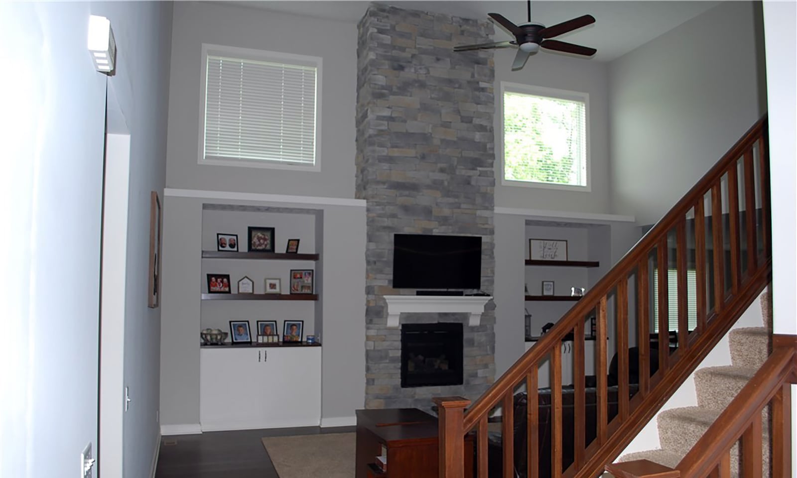 The great room has a floor to ceiling stone fireplace, neutral carpeting and hardwood flooring and built in bookcases.