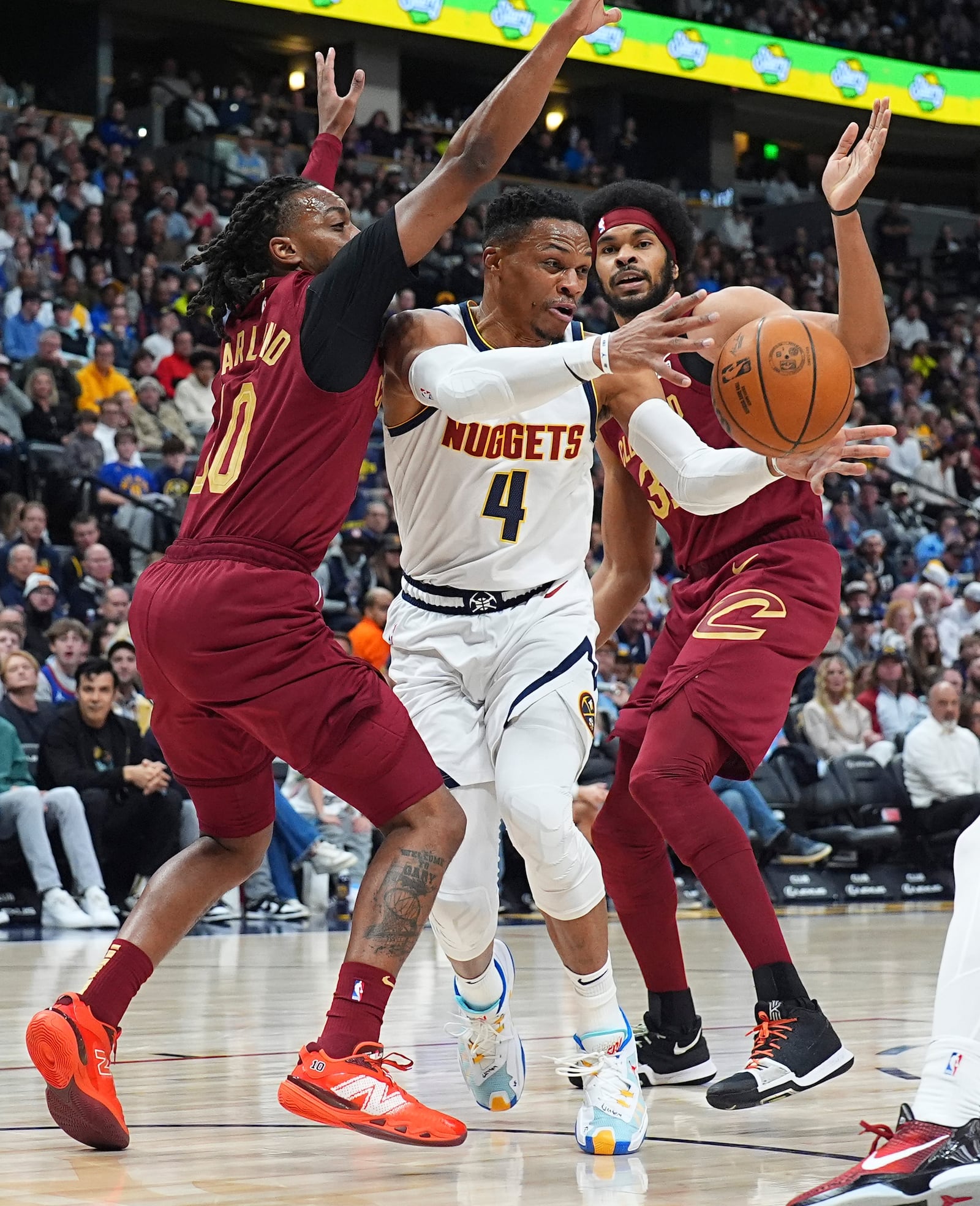 Denver Nuggets guard Russell Westbrook, center, passes the ball as he drives between Cleveland Cavaliers guard Darius Garland, left, and center Jarrett Allen in the first half of an NBA basketball game Friday, Dec. 27, 2024, in Denver. (AP Photo/David Zalubowski)