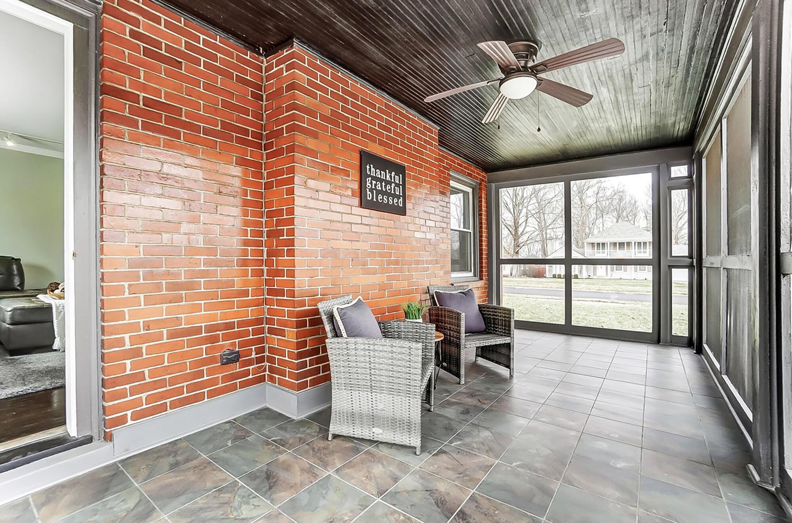 The screened porch on the side of the house is off the living room. It has tile flooring and a ceiling fan.