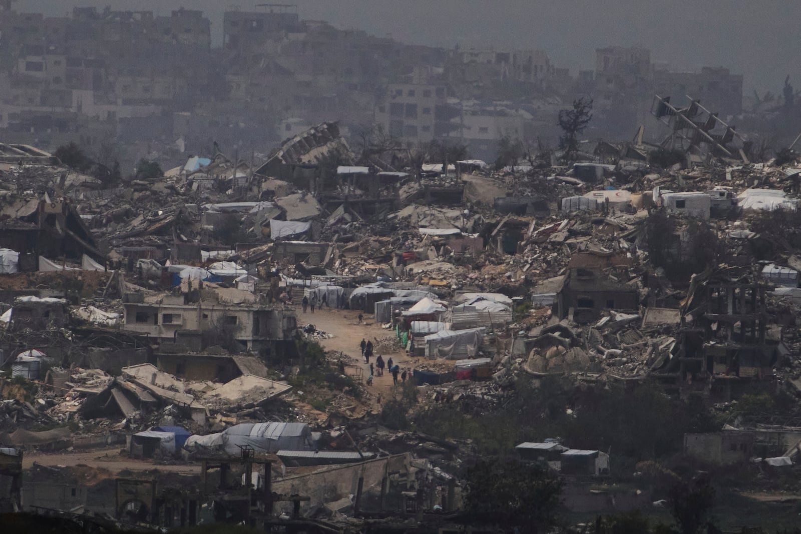 People walking surrounded by buildings destroyed during the Israeli air and ground offensive in the Gaza Strip are seen from southern Israel, Thursday, March 20, 2025. (AP Photo/Leo Correa)