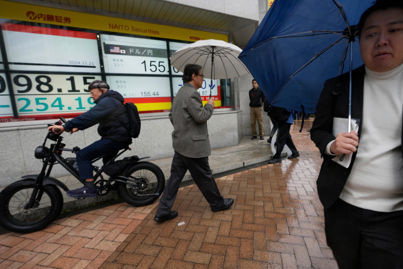 People walk by monitors showing Japan's Nikkei 225 index and Japan's foreign exchange rate against the U.S. dollar at a securities firm in Tokyo, Thursday, Nov. 21, 2024. (AP Photo/Hiro Komae)