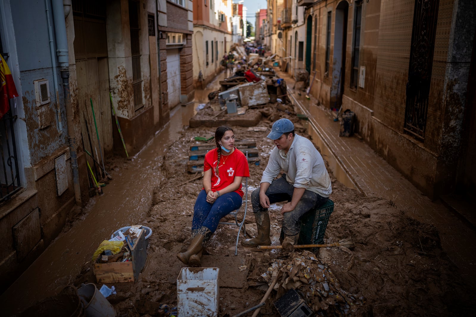 Volunteers take a break while clearing mud from the streets in an area affected by floods in Paiporta, Valencia, Spain, Tuesday, Nov. 5, 2024. (AP Photo/Emilio Morenatti)