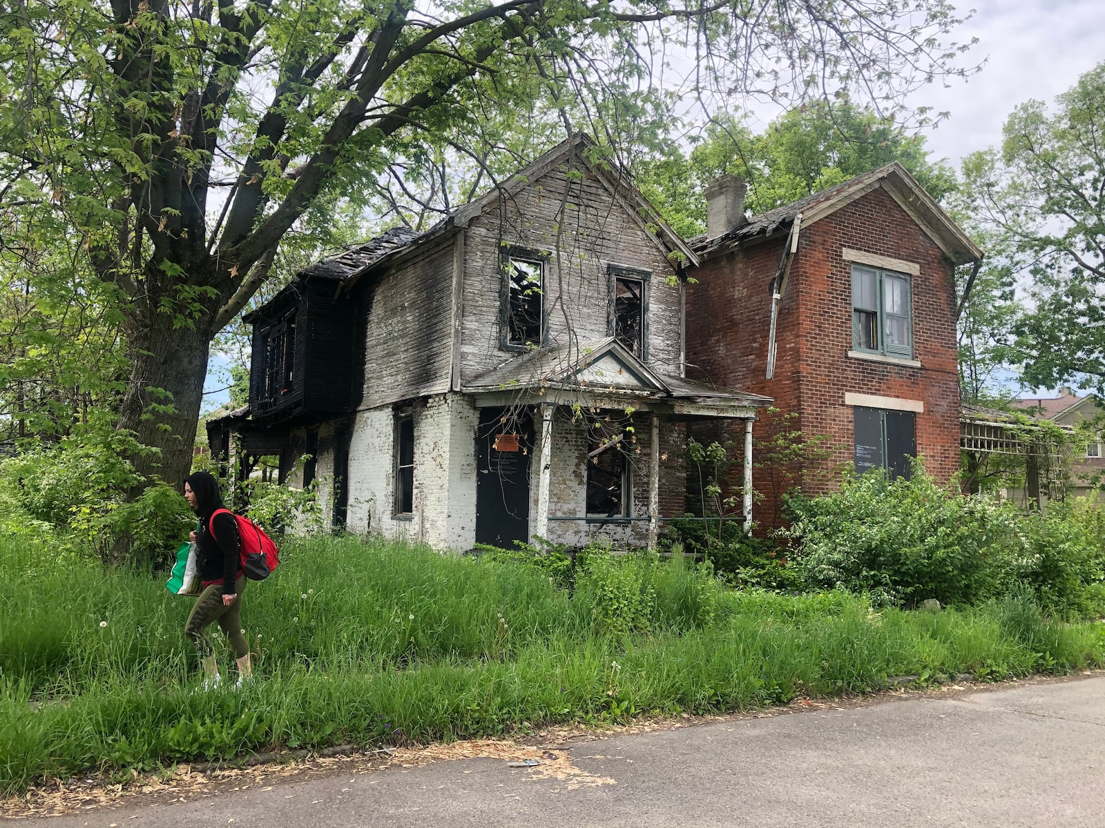 Dayton plans to demolish about 850 housing units using more than $15 million in federal rescue funds. A woman walks by two abandoned and vacant homes in East Dayton. CORNELIUS FROLIK / STAFF