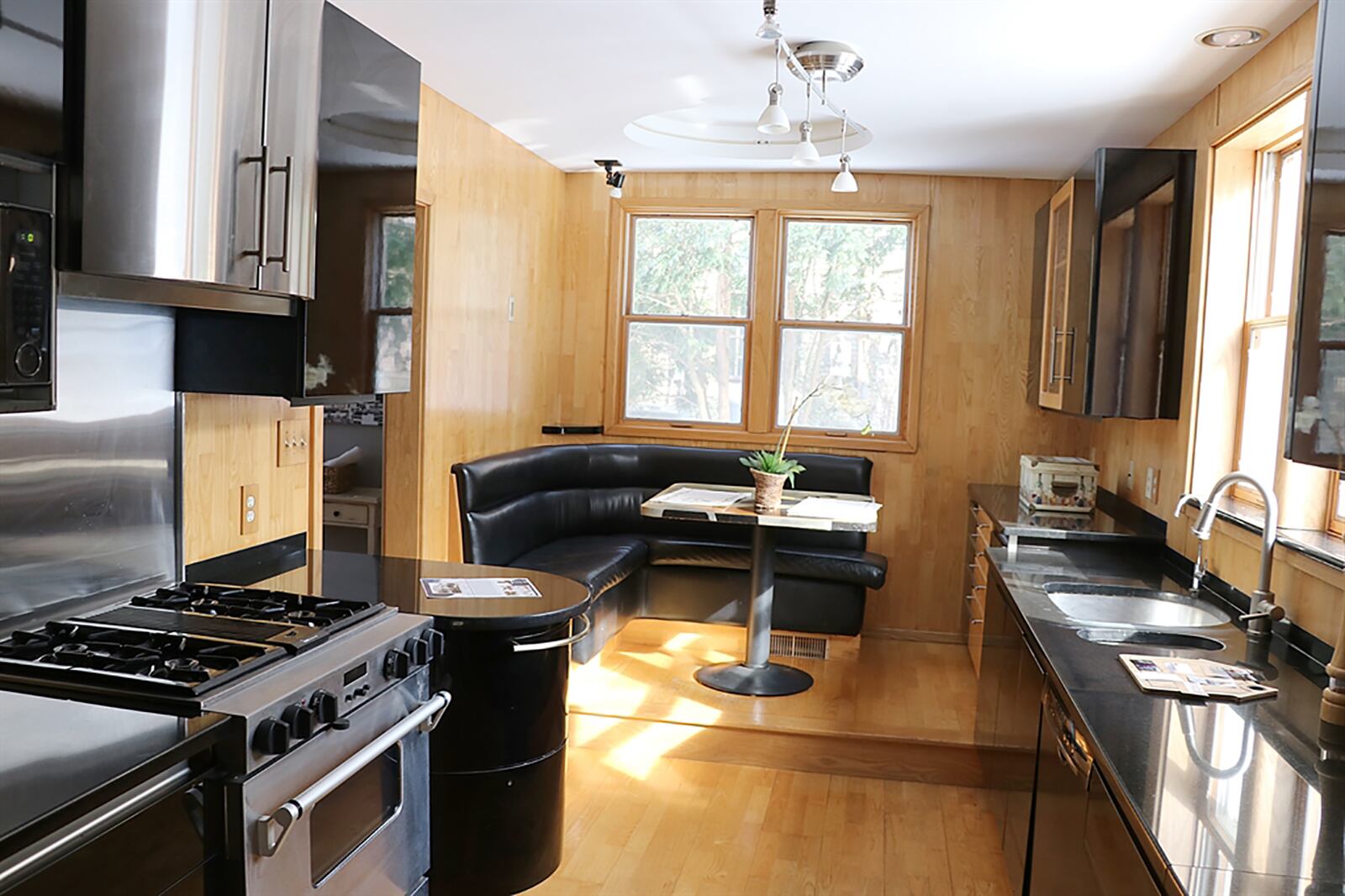 The contemporary kitchen has polished black cabinetry and stainless-steel appliances. Complementing black countertops extend into the elevated breakfast nook, which has built-in seating and table. CONTRIBUTED PHOTO BY KATHY TYLER