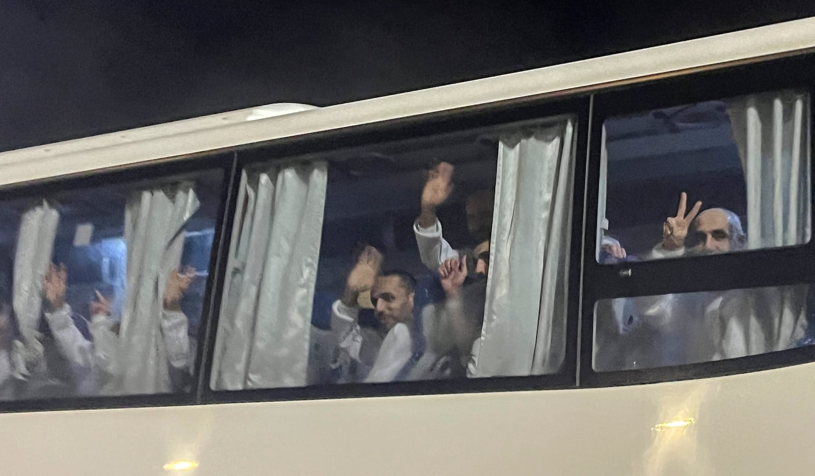 Palestinian prisoners deported outside the Palestinian Territories, wave after being released from Israeli prison, following a ceasefire agreement between Israel and Hamas, as they arrive at the Egyptian side of the Rafah border crossing between Egypt and the Gaza Strip, Thursday, Feb. 27, 2025. (AP Photo/Mohamed Arafat)