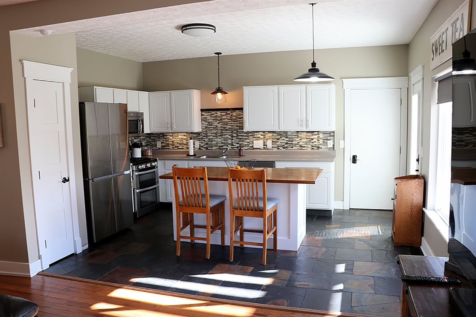 Tucked off the living room is the kitchen with white cabinetry and complementing countertops. A large island has a butcher-block countertop, under-counter storage and breakfast bar seating for up to four. The kitchen has a slate floor and updated light fixtures. CONTRIBUTED PHOTO BY KATHY TYLER