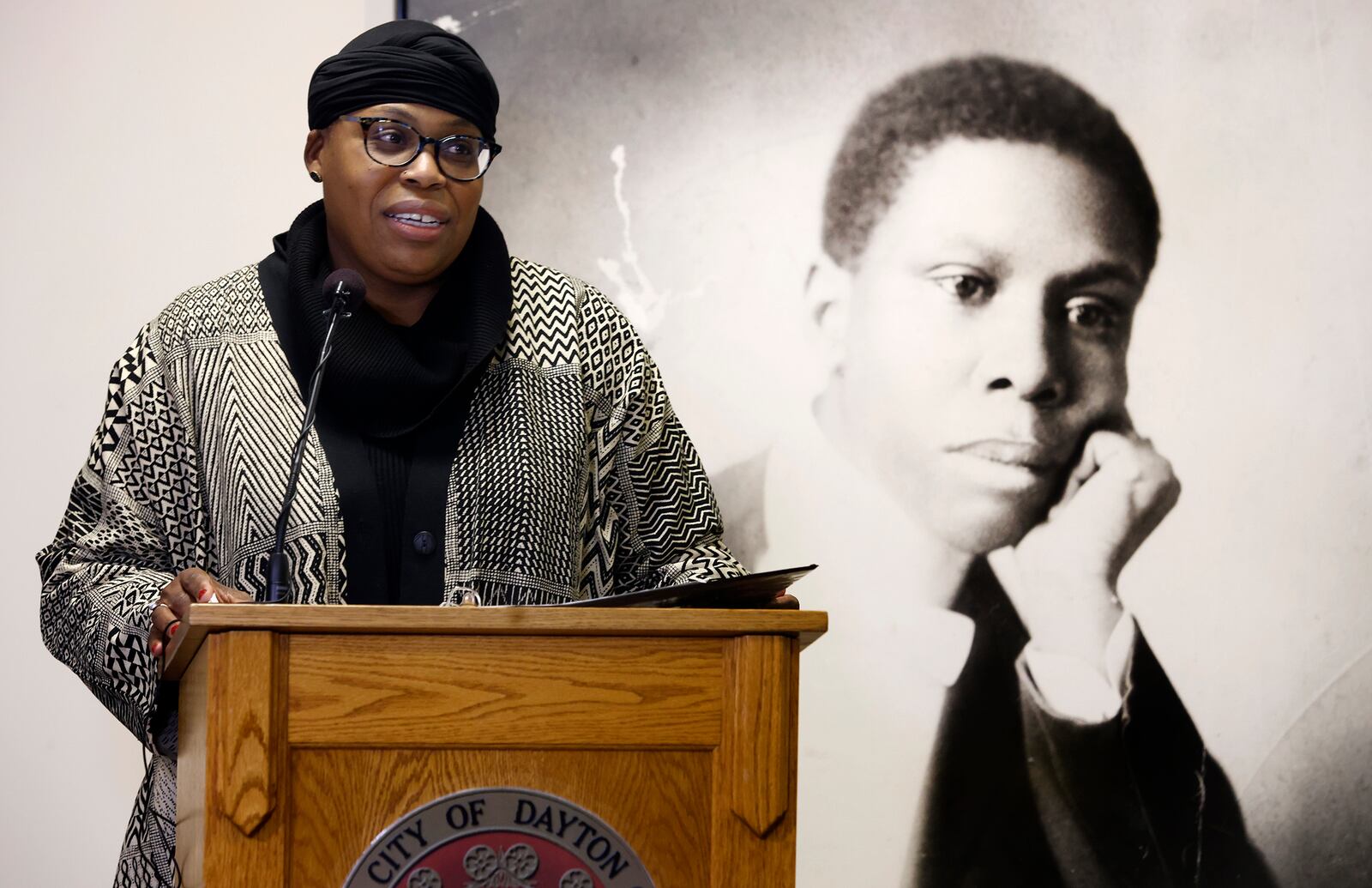 Sierra Leone, Dayton's first poet laureate, stands in front of a photo of Paul Laurence Dunbar Friday, Feb. 7, 2025 at a  media event at the Paul Laurence Dunbar House Visitor Center. MARSHALL GORBY\STAFF