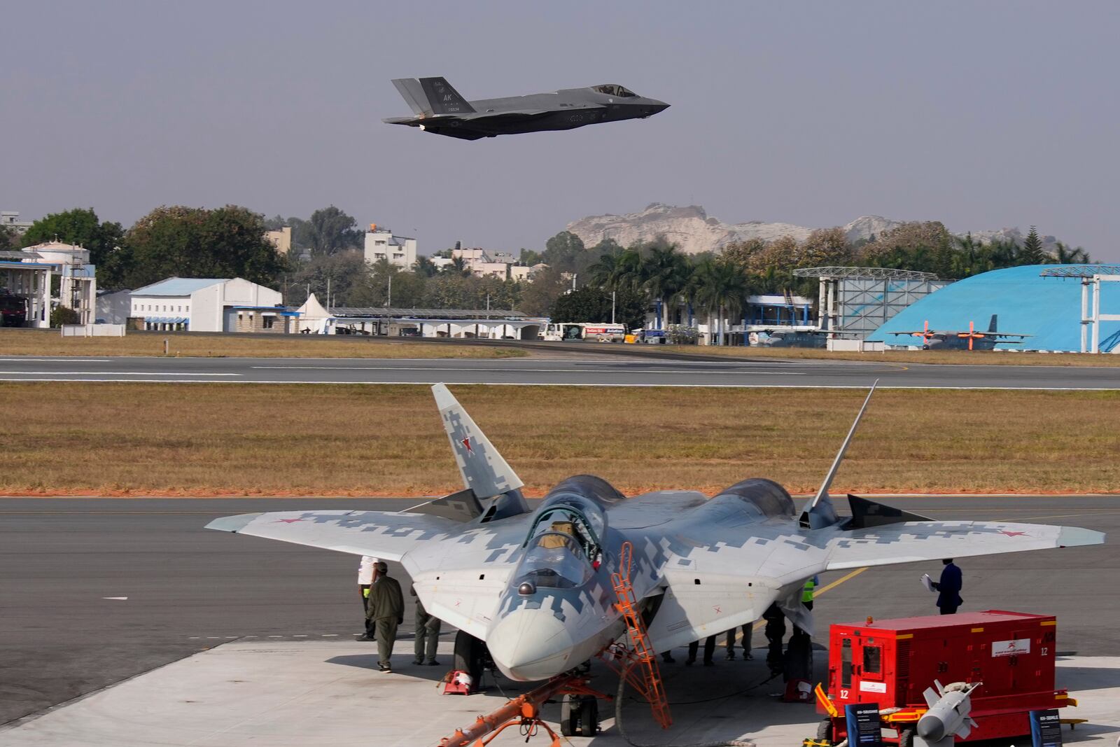 U.S. Air Force fighter aircraft F-35 flies over Russia's Su-57 fighter aircraft, parked at the static display area, on the fourth day of the Aero India 2025, a biennial event, at Yelahanka air base in Bengaluru, India, Thursday, Feb. 13, 2025. (AP Photo/Aijaz Rahi)