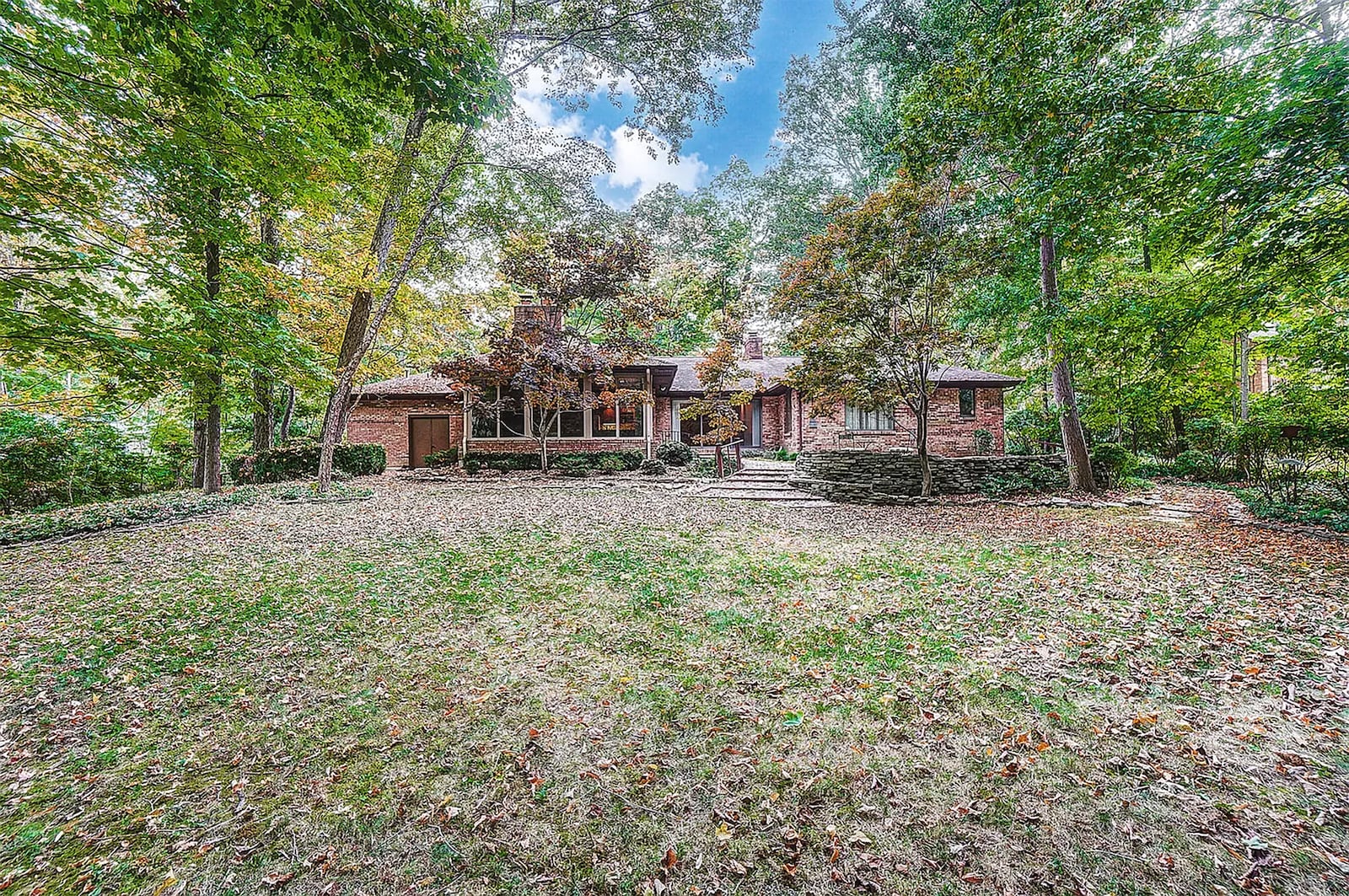 The rear of the home features stone retaining walls, multiple patios in stone and brick and mature trees. The yard has a wood fence at the rear.