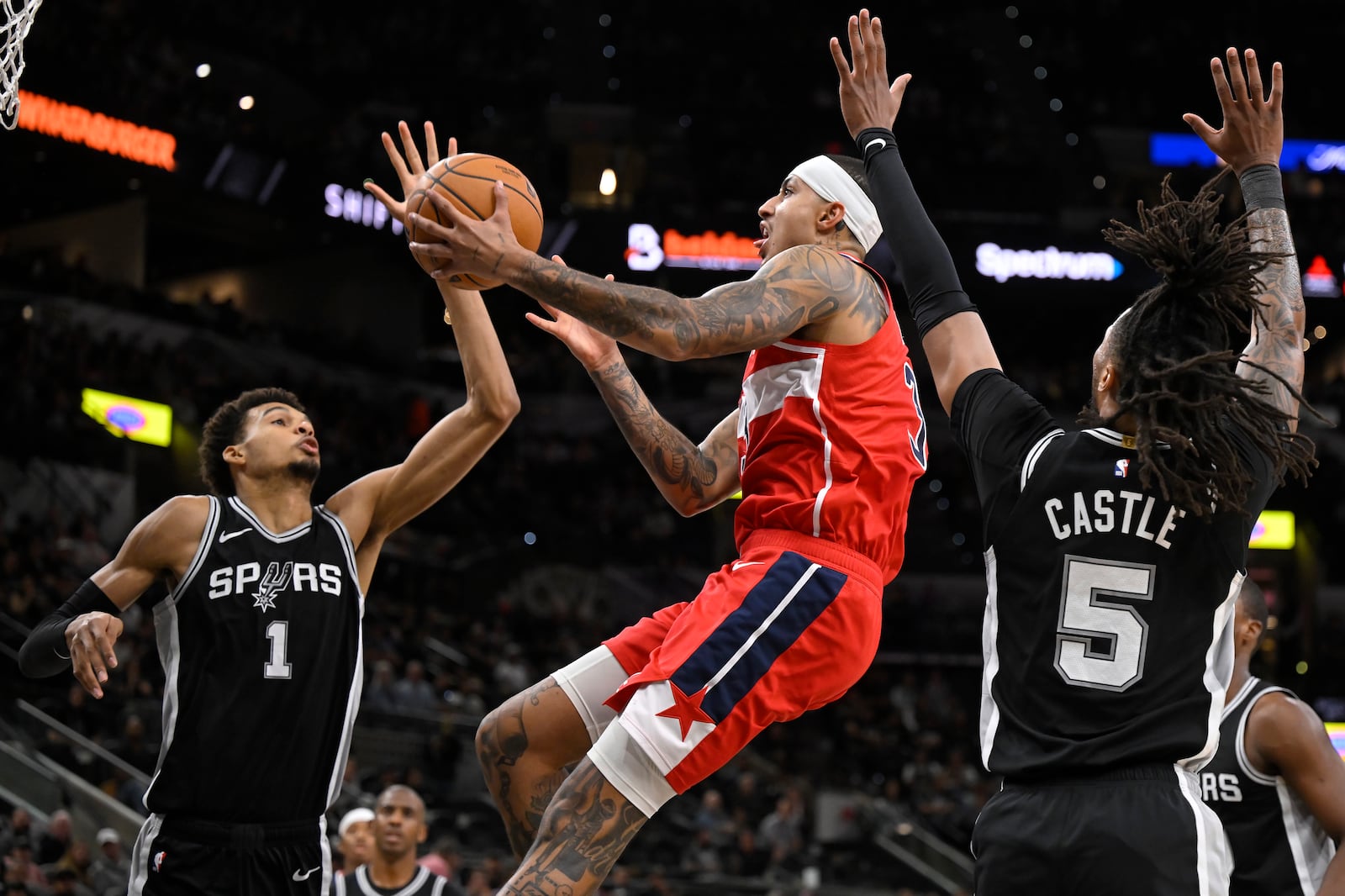 Washington Wizards' Kyle Kuzma, center, goes to the basket against San Antonio Spurs' Victor Wembanyama (1) and Stephon Castle during the first half of an NBA basketball game, Thursday, Nov. 13, 2024, in San Antonio. (AP Photo/Darren Abate)