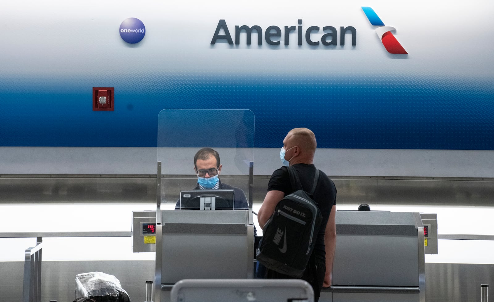 FILE — A masked passenger checks in with an American Airlines employee who is masked, and also behind a screen, at Miami International Airport in Miami on June 7, 2020. American Airlines warned employees on Tuesday, Aug. 25, 2020, that it will furlough up to 19,000 workers on Oct. 1, saying that there is no sign that the pandemic-induced fear of travel is diminishing. (Josh Ritchie/The New York Times)